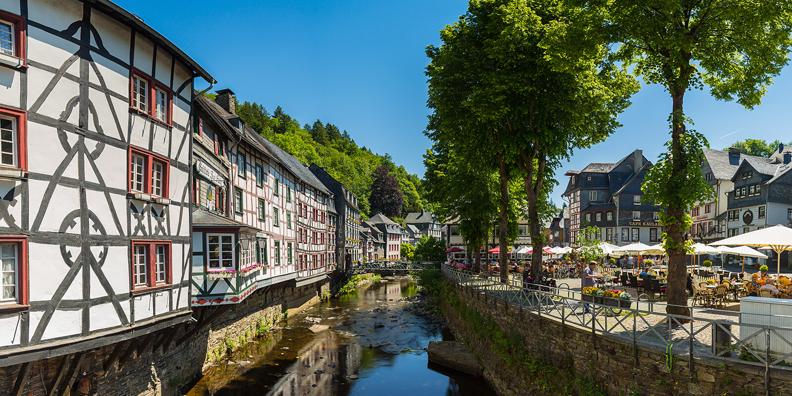 Bach durch Dorf mit Fachwerkhäusern und Cafés am Sonnentag.