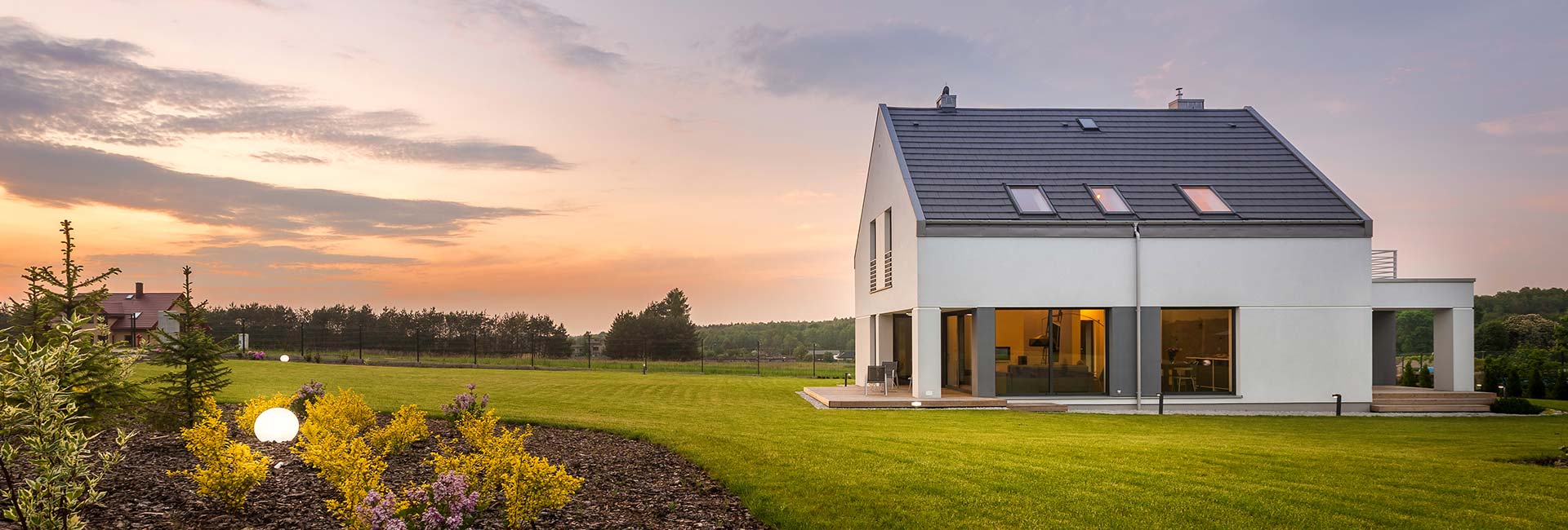 Weißes Haus mit großen Fenstern auf grünem Rasen bei Sonnenuntergang, Vorgarten.