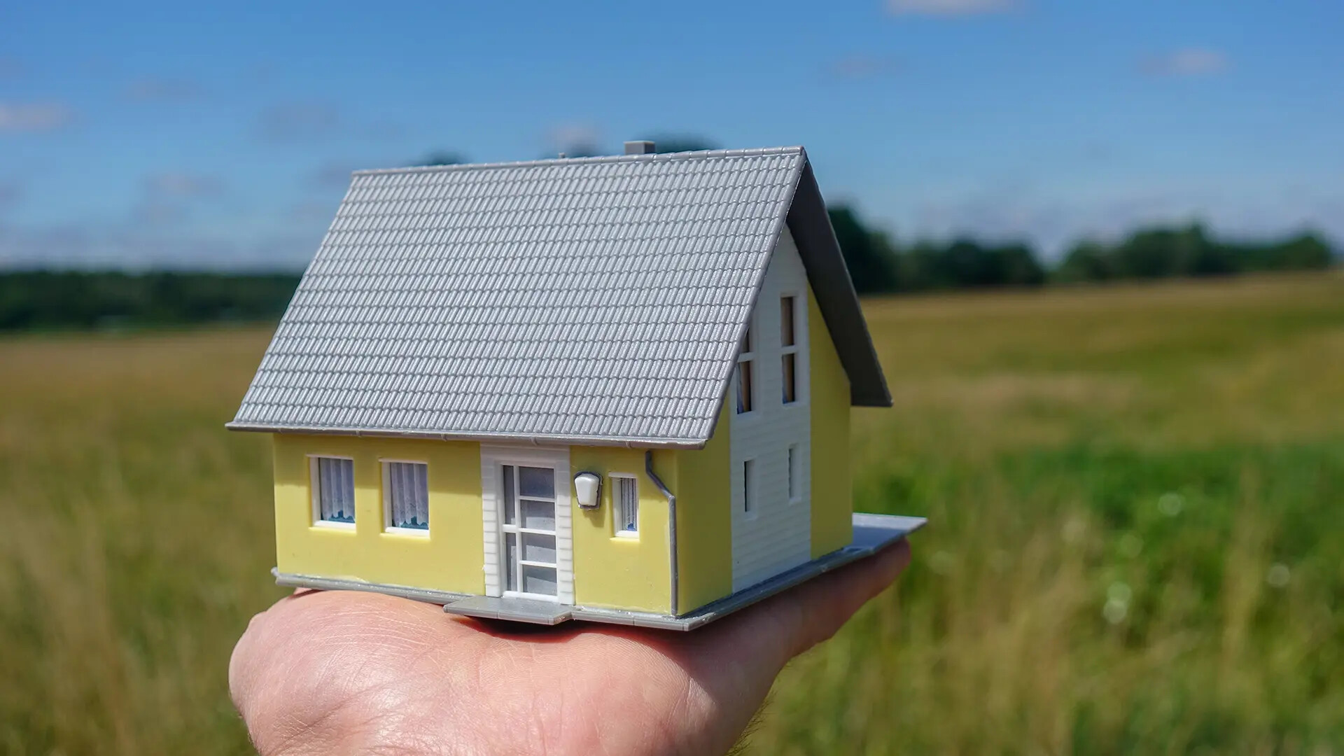 Hausmodell in Hand vor Grundstück