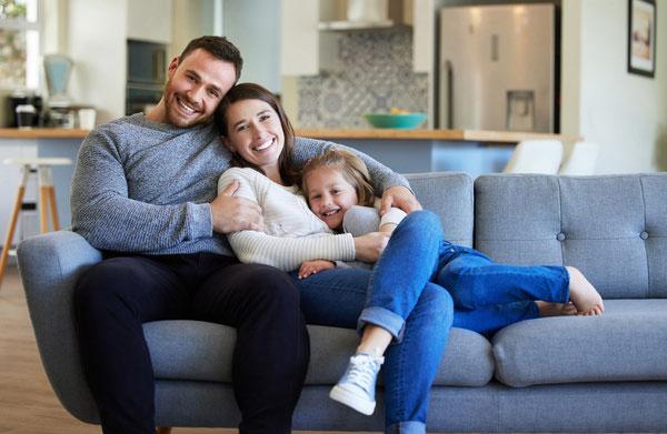 Glückliche junge Familie entspannt gemeinsam auf einem modernen grauen Sofa.