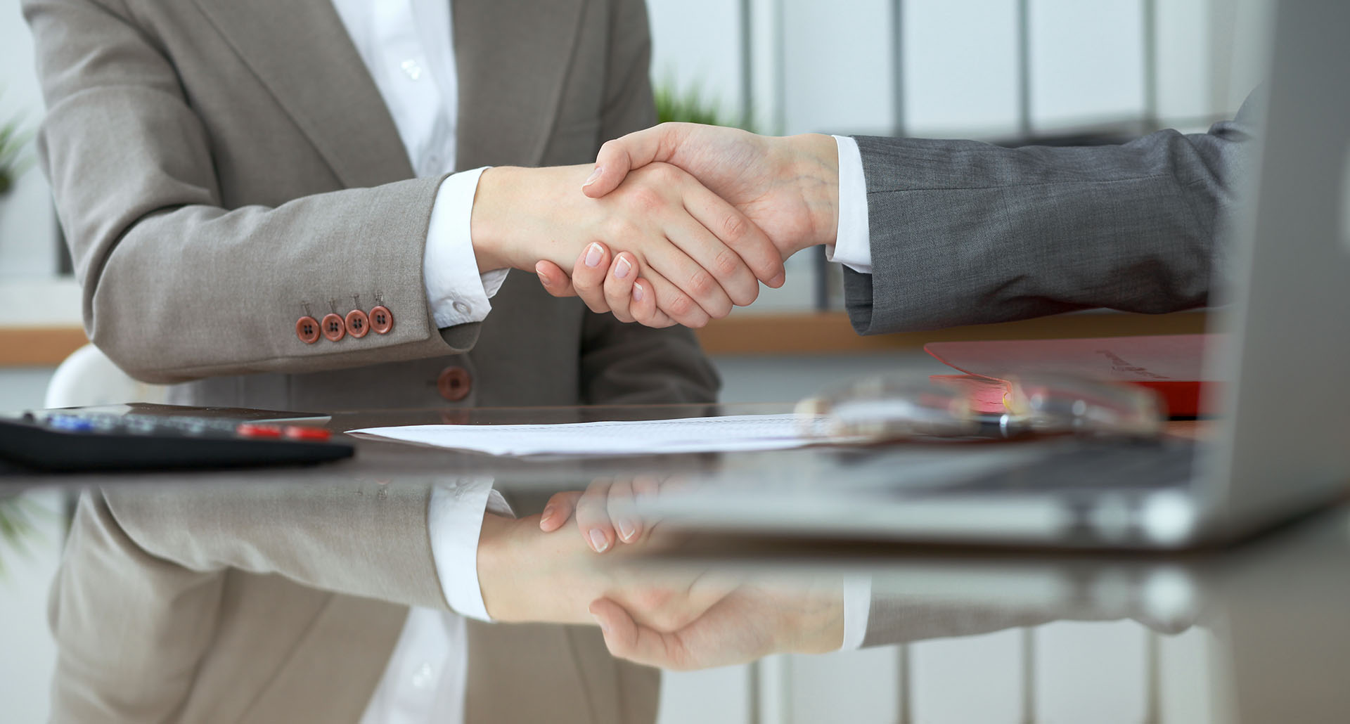 Zwei Personen im Anzug geben sich am Schreibtisch die Hand.