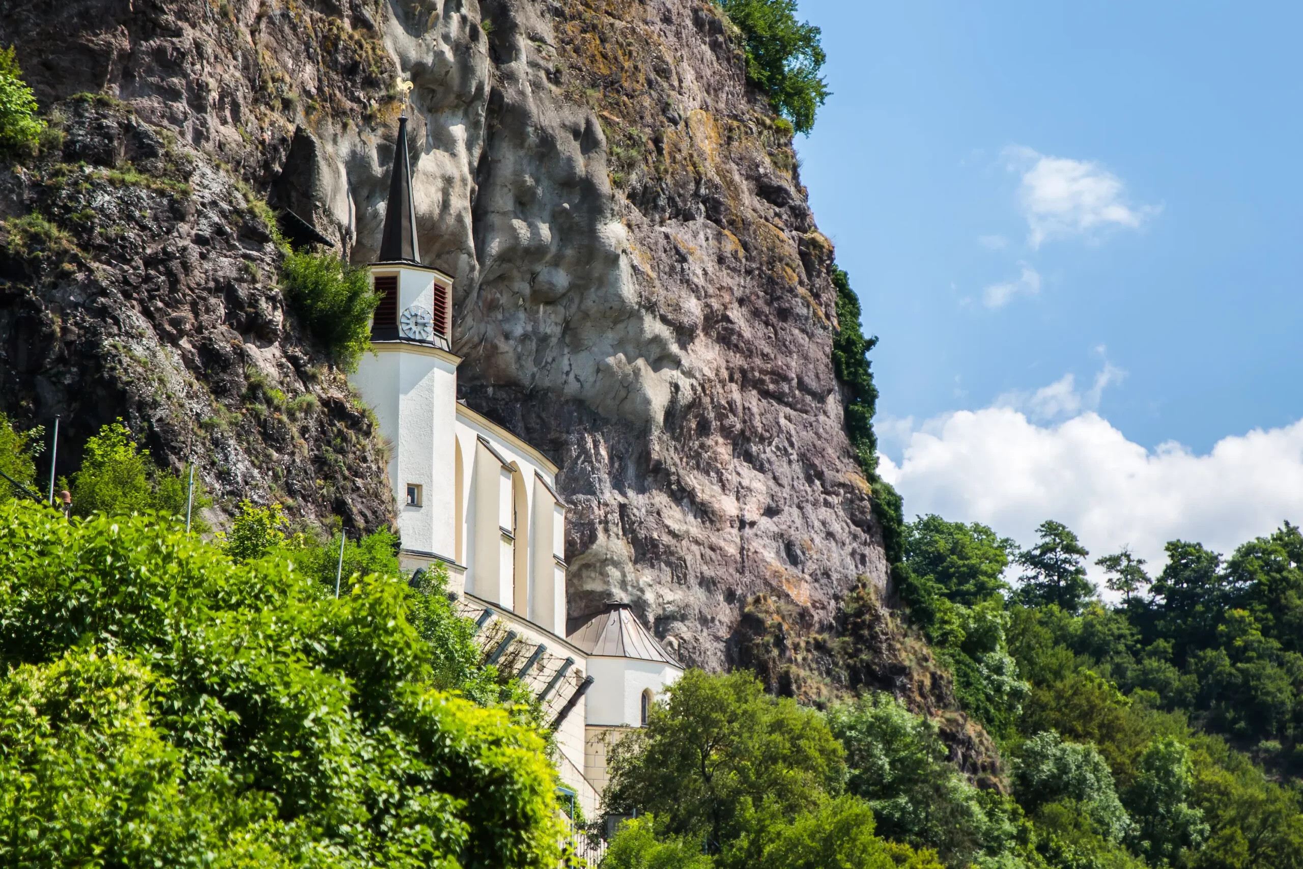 Weiße Kirche in felsiger Steilküste, grüne Bäume, blauer Himmel.