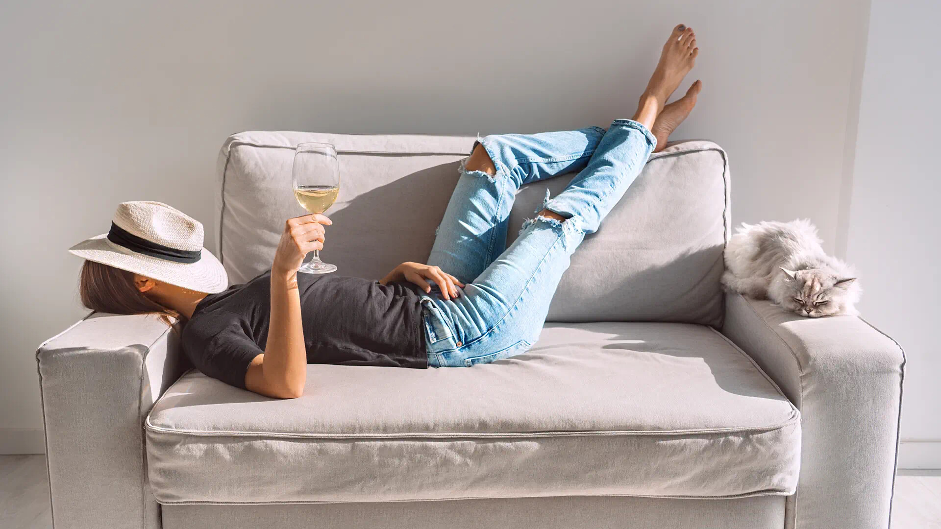 Frau mit Wein und Hut auf Sofa mit Katze
