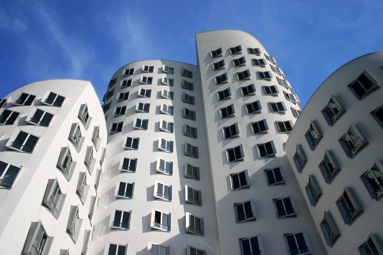 Weiße, gebogene Fassade mit vielen Fenstern vor blauem Himmel.