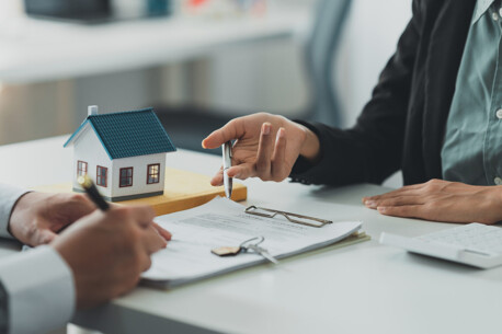 Zwei Personen unterschreiben Immobilienunterlagen am Schreibtisch.