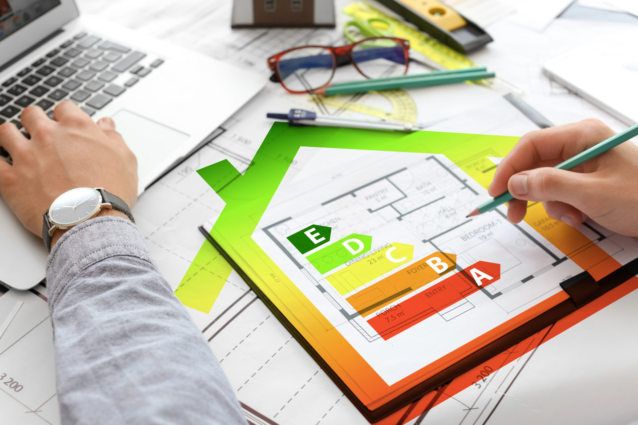 Person mit Hausplan und Energieeffizienzskala A-E am Laptop.