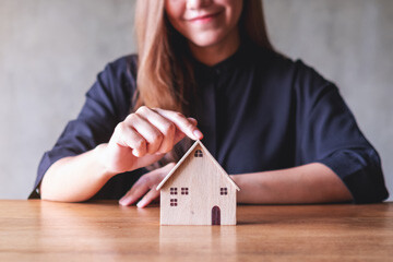 Frau berührt das Dach eines kleinen Holzhaus-Modells auf Tisch.