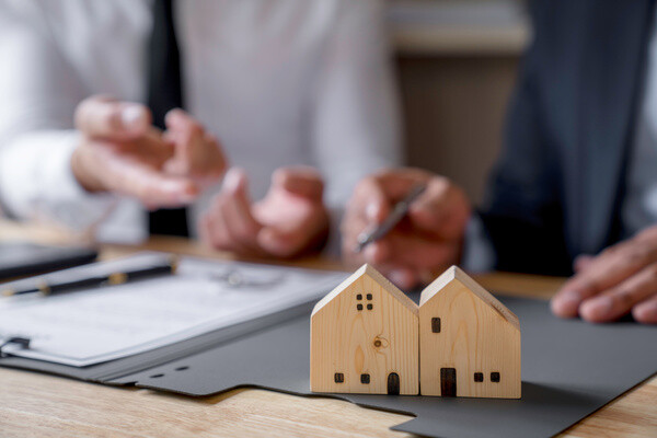 Zwei Personen besprechen Dokumente, vor ihnen zwei Holzhausmodelle.