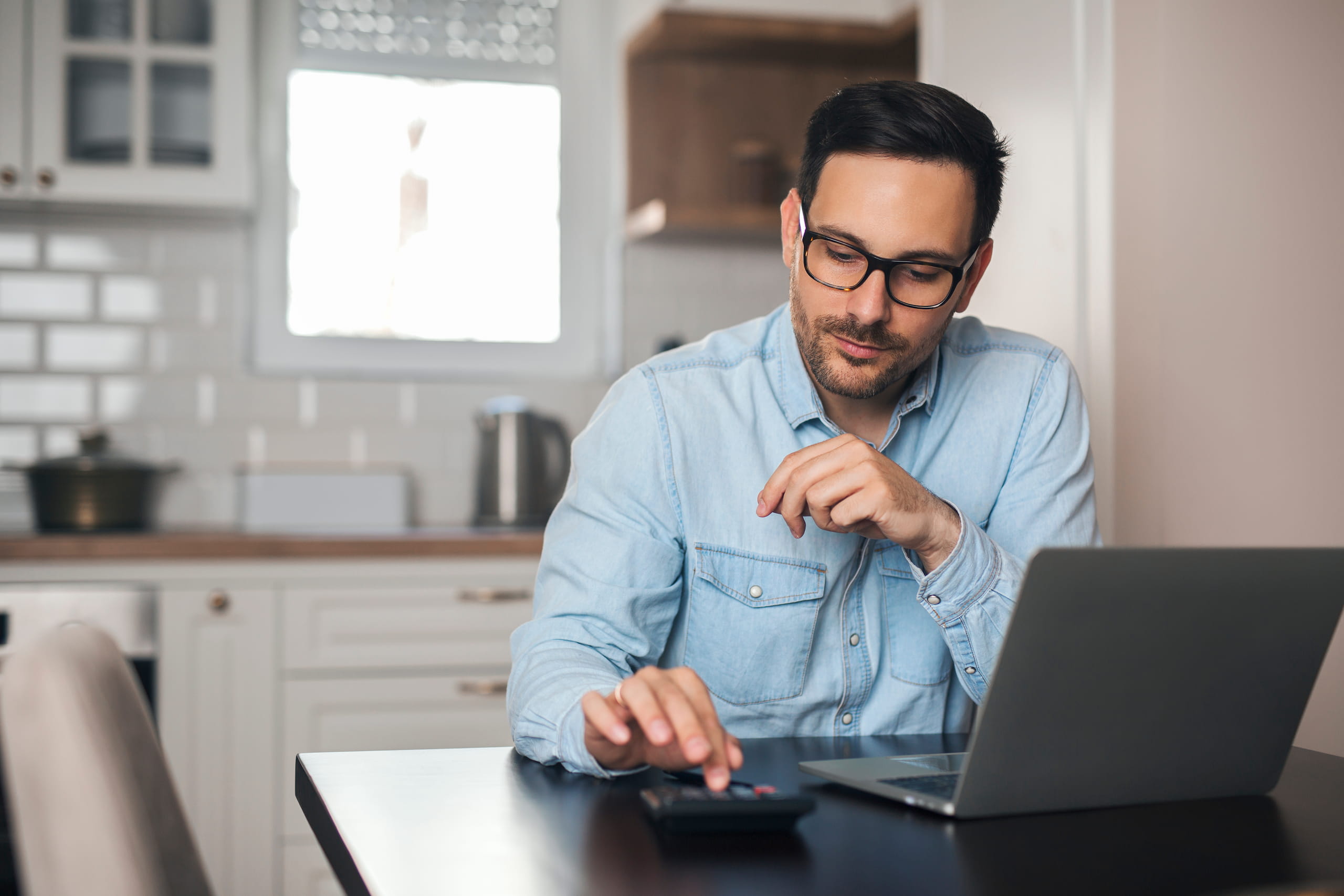 Mann mit Brille arbeitet konzentriert mit Rechner und Laptop am Tisch.