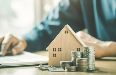 Holzhaus, Münzen, Hausschlüssel und Laptop im Hintergrund.