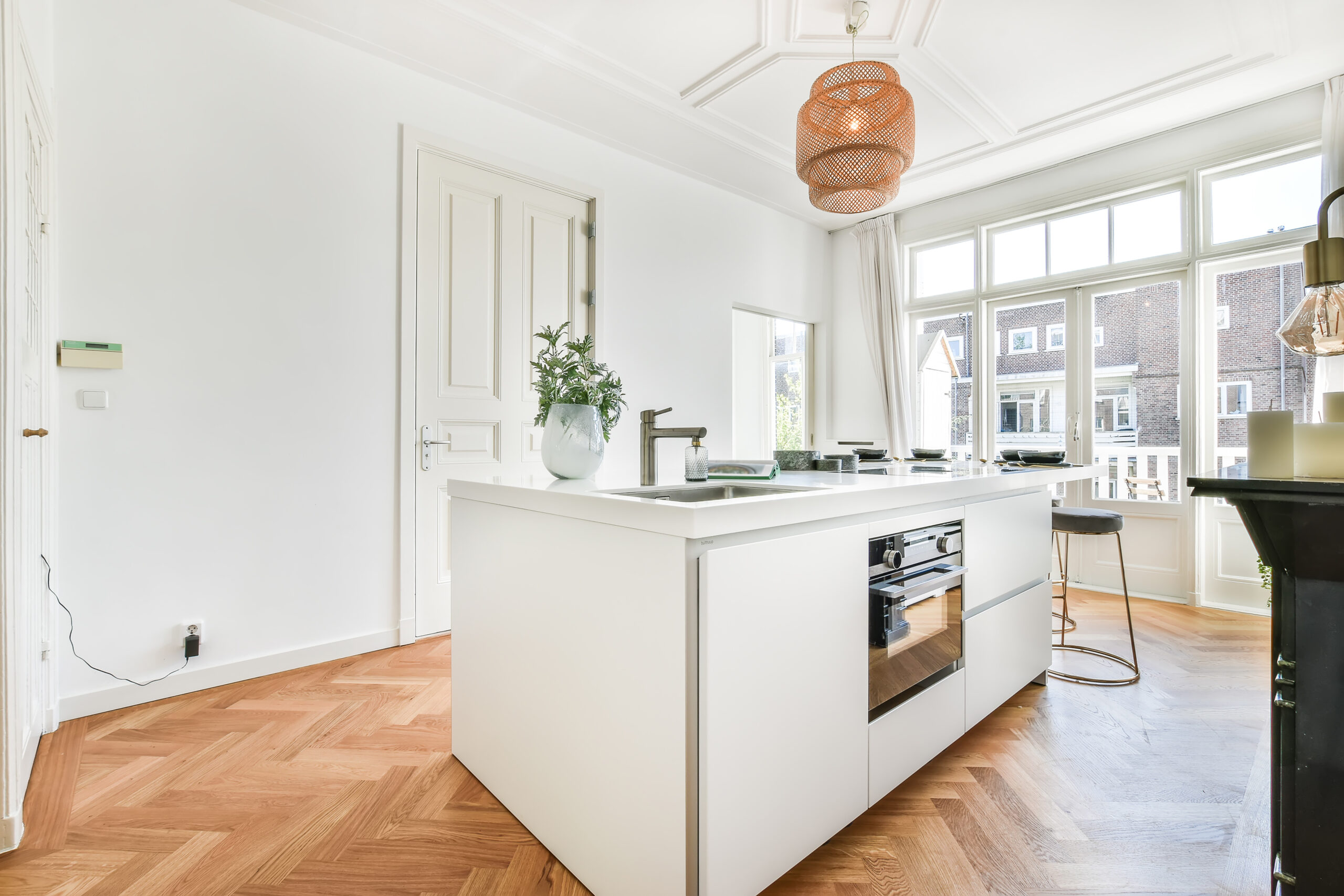 Moderne Küche mit weißer Insel, Holzfußboden und großen Fenstern.