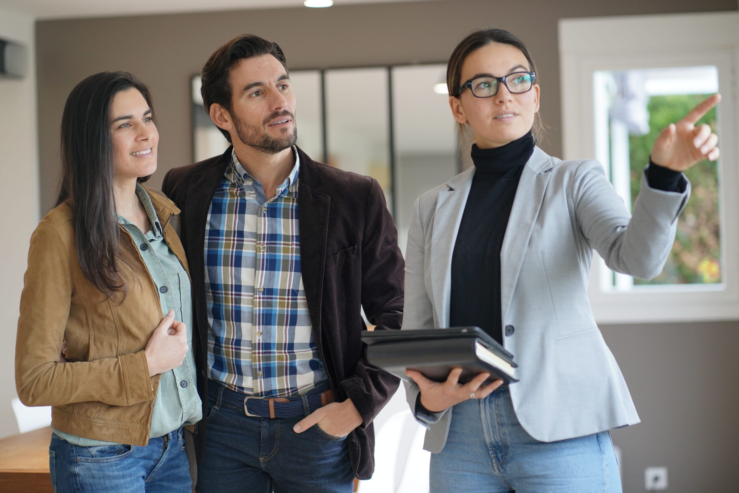Makler zeigt jungem Paar etwas in modernem Haus.