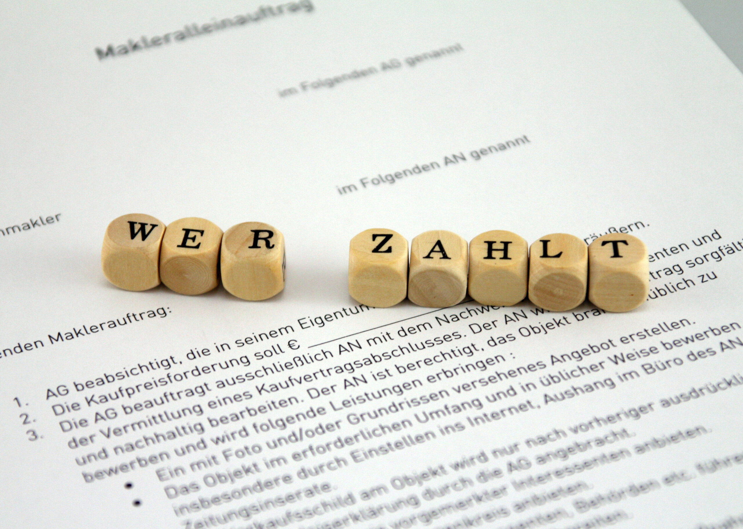 Holzbuchstaben "WER ZAHLT" auf deutschem Vertrag.