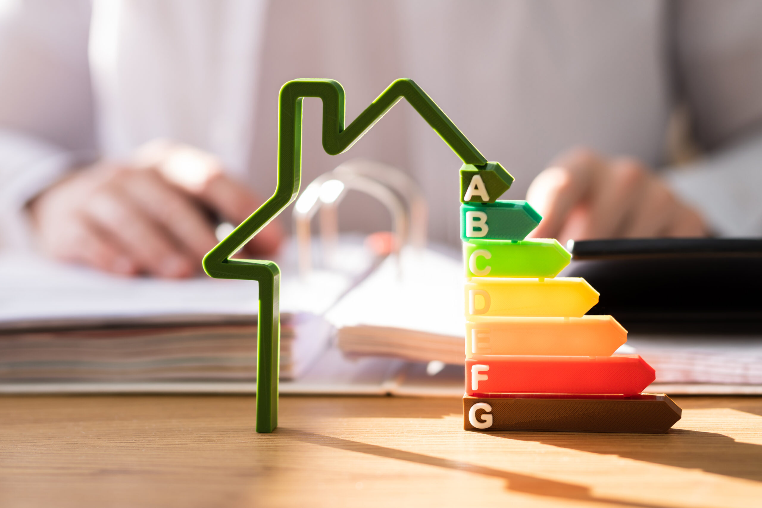 Person am Schreibtisch, Hausrahmen, bunte Energieeffizienz-Balken.