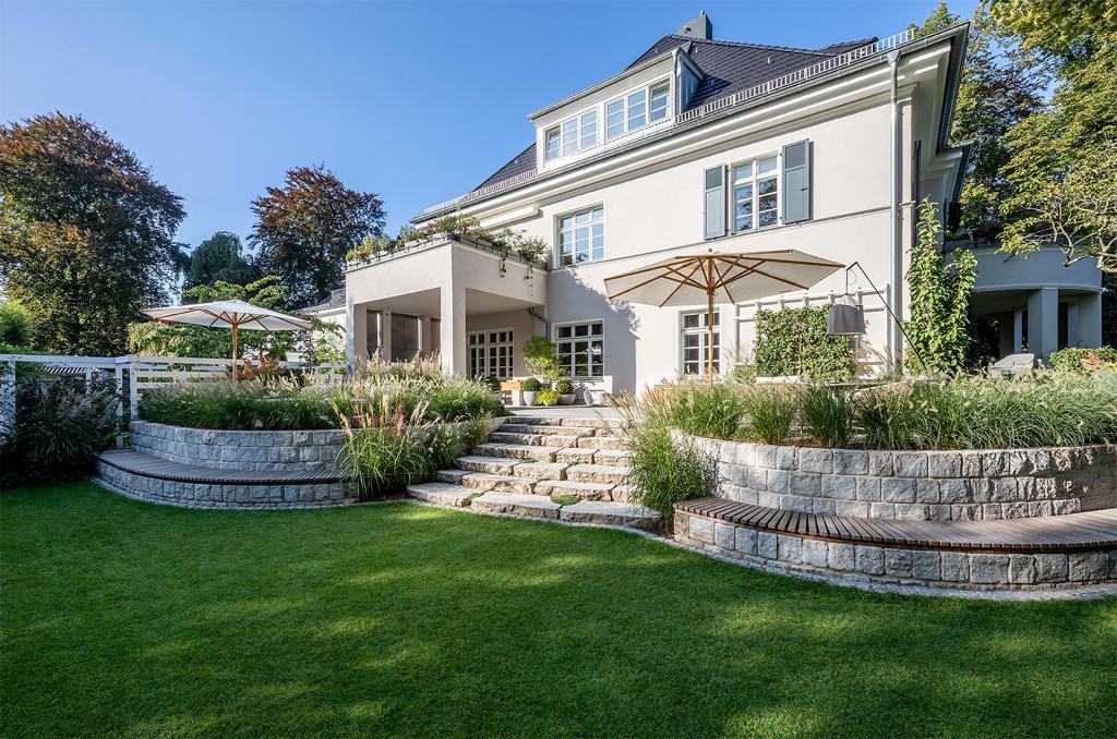 Gartenansicht einer großzügigen Villa mit Terrasse und Sonnenschirmen in der Sonne