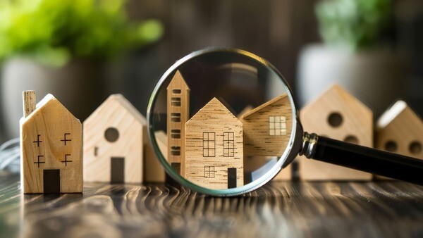 Eine Lupe richtet sich auf Miniaturhäuser aus Holz