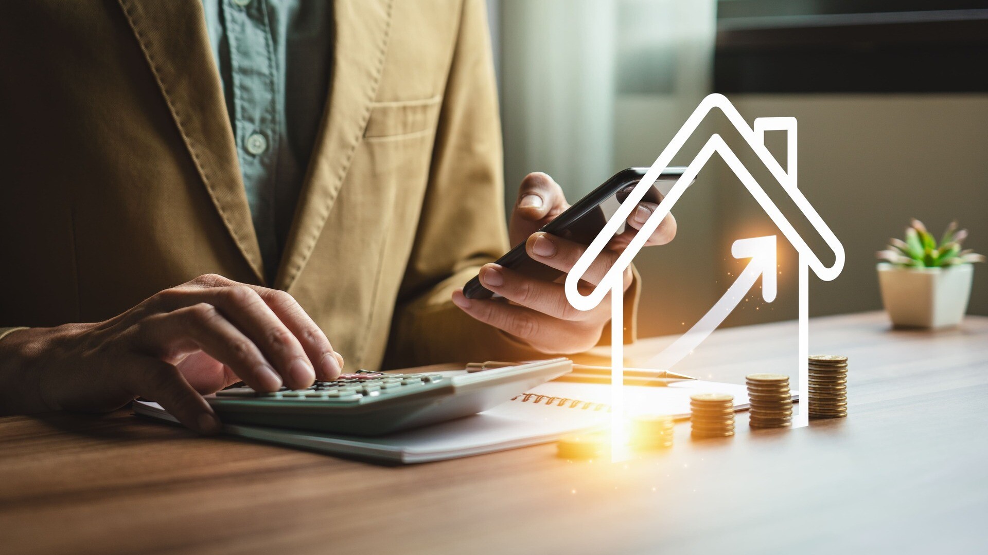 Person sitzt am Schreibtisch mit einem Taschenrechner, davor ein digitales Haus mit Münzstapeln