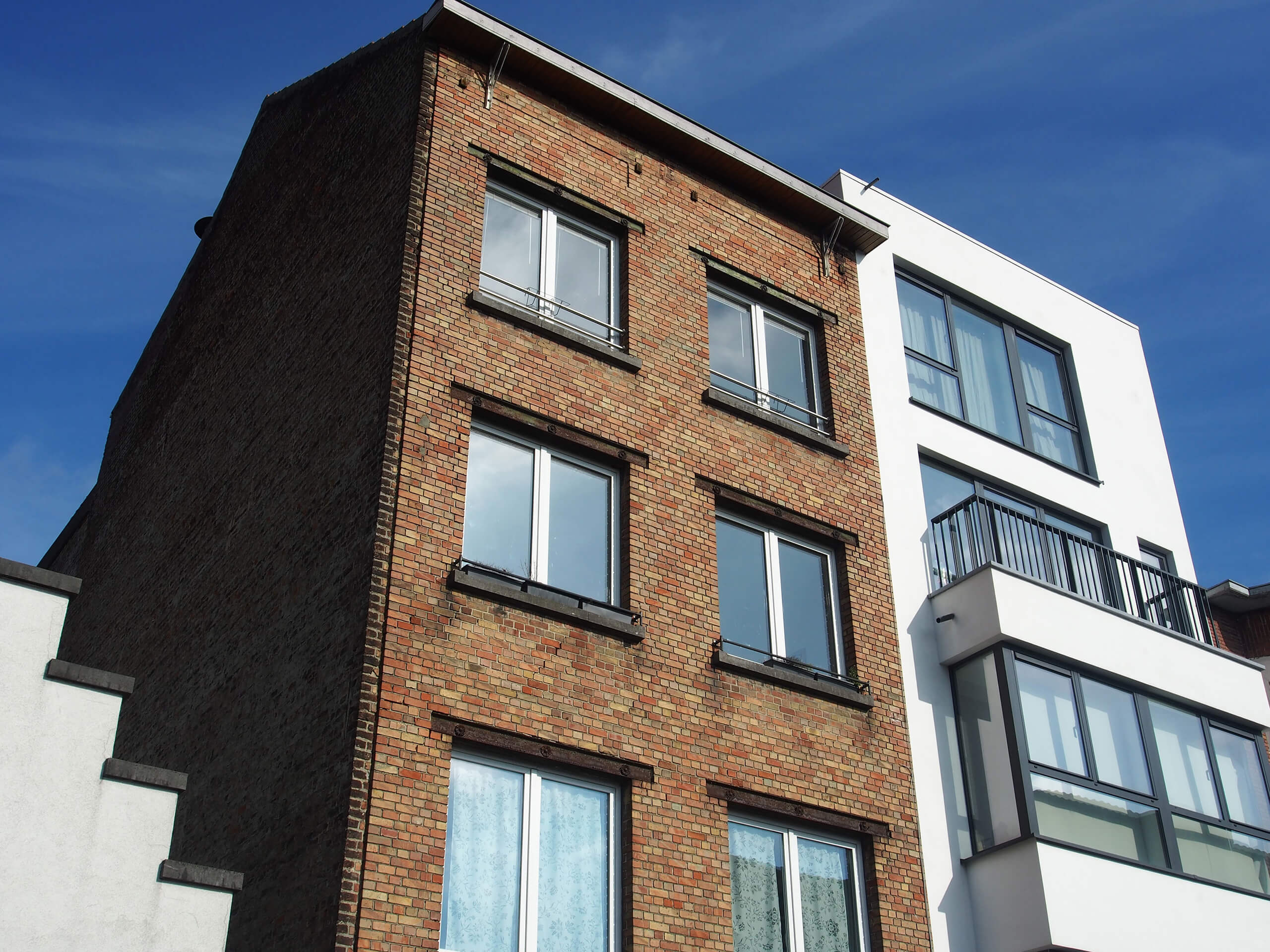 Zwei Wohnhäuser, eines aus Backstein, eines weiß, vor blauem Himmel: Neubau oder Bestandsimmobilie?