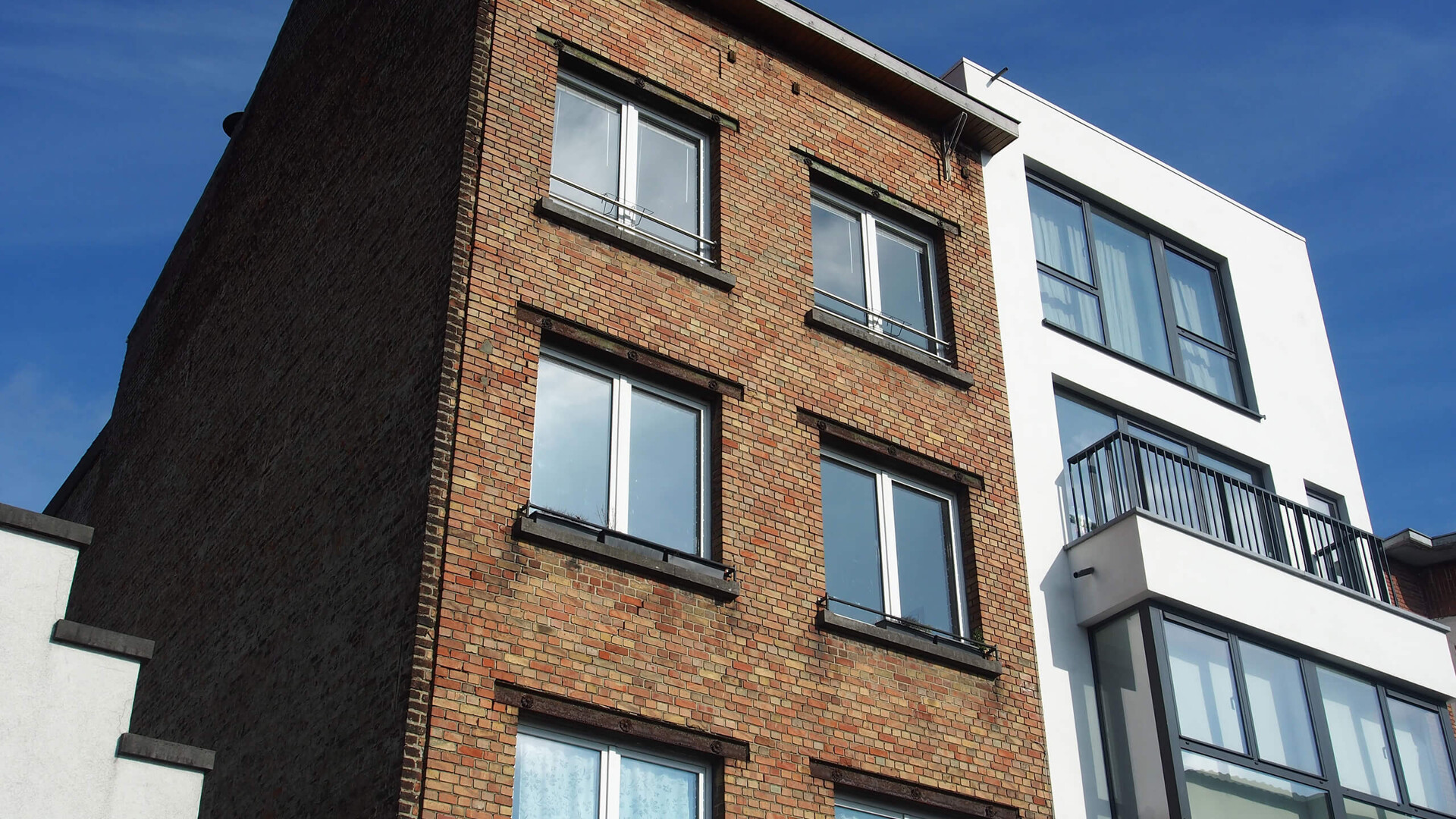 Zwei Wohnhäuser, eines aus Backstein, eines weiß, vor blauem Himmel: Neubau oder Bestandsimmobilie?