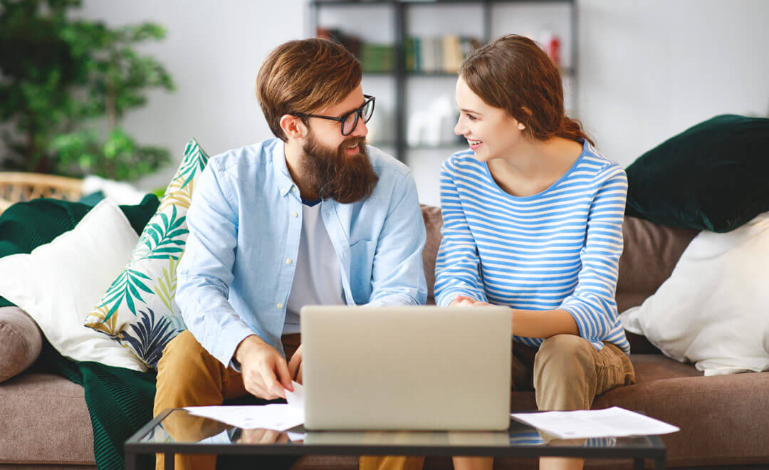 Junges Paar im Wohnzimmer mit Laptop und Unterlagen für die Finanzierung
