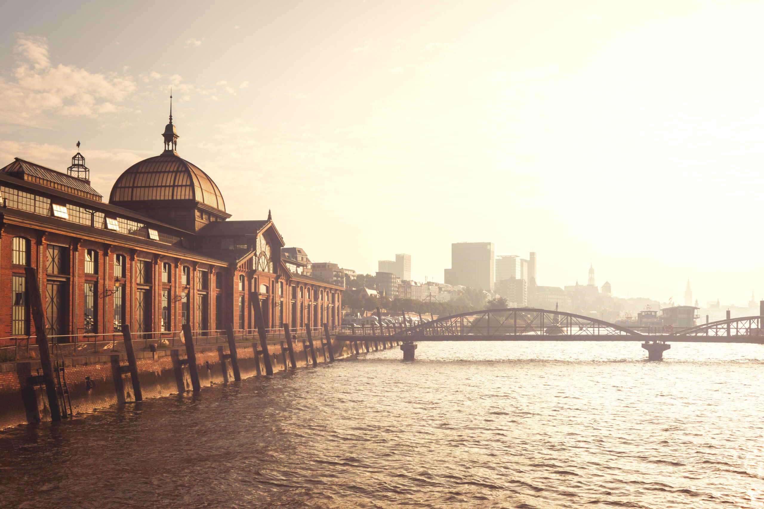 Backsteingebäude mit Kuppel am Wasser, Skyline und Brücke bei Sonnenuntergang.