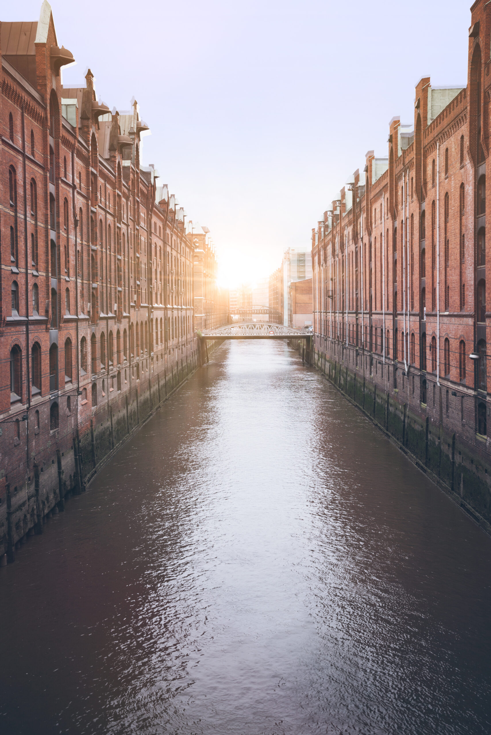 Kanal mit roten Backsteingebäuden bei Sonnenuntergang, Brücke in der Ferne.