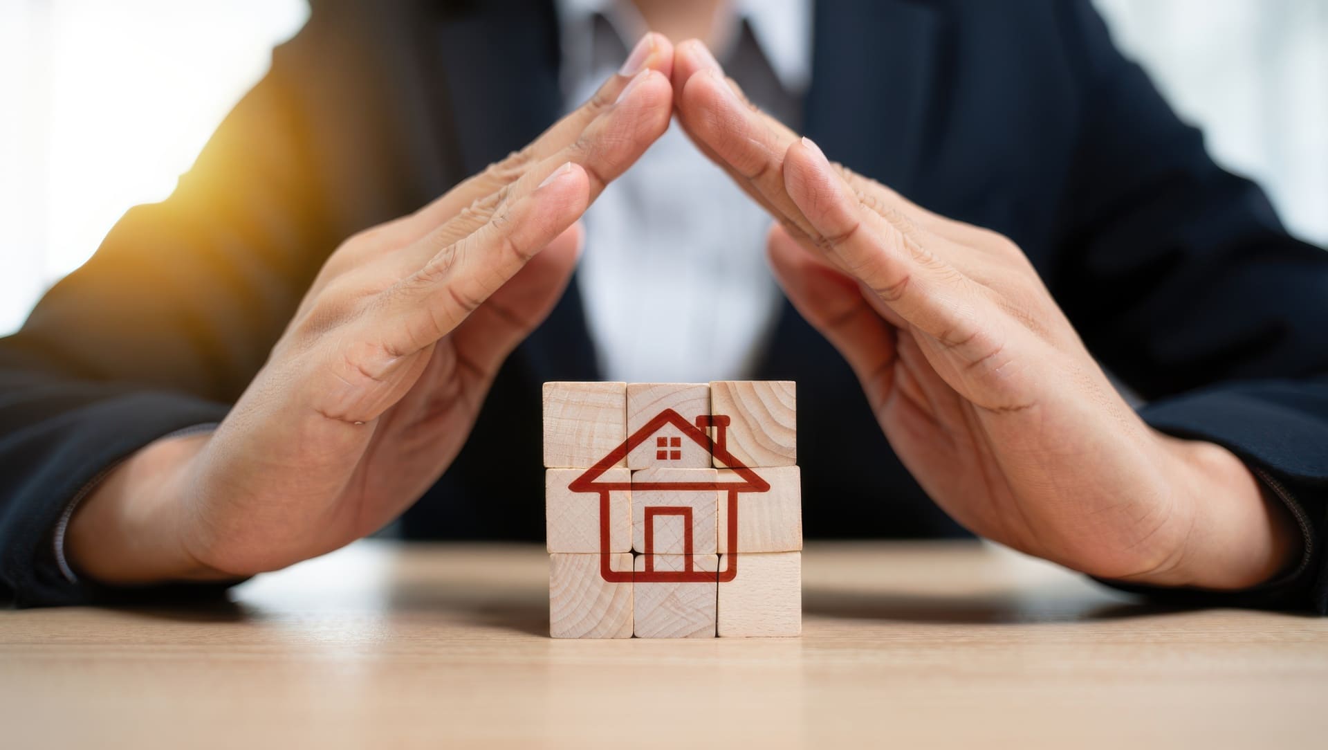 Hände formen ein Dach über Haus-Symbol auf Würfeln.