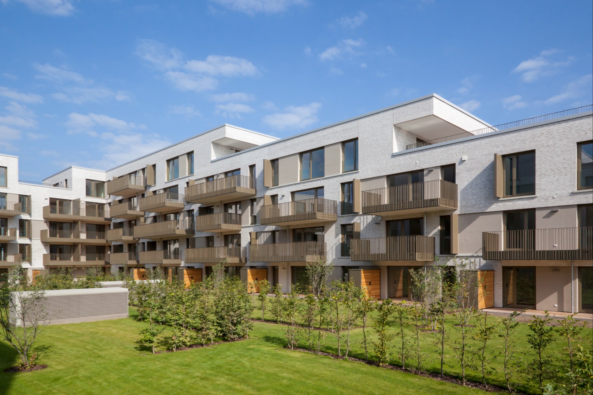 Moderner Mehrfamilienhaus-Neubau mit Balkonen und gepflegtem grünem Innenhof.