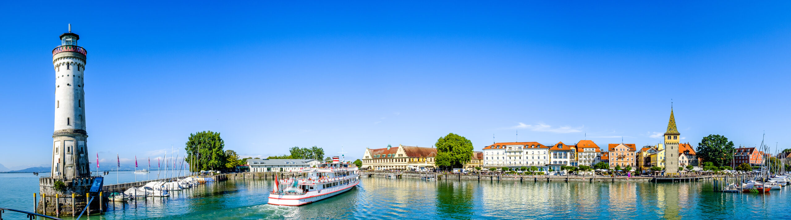 Panoramablick auf den Hafen von Lindau mit dem Leuchtturm, Passagierschiff und historischen Gebäuden am Bodensee