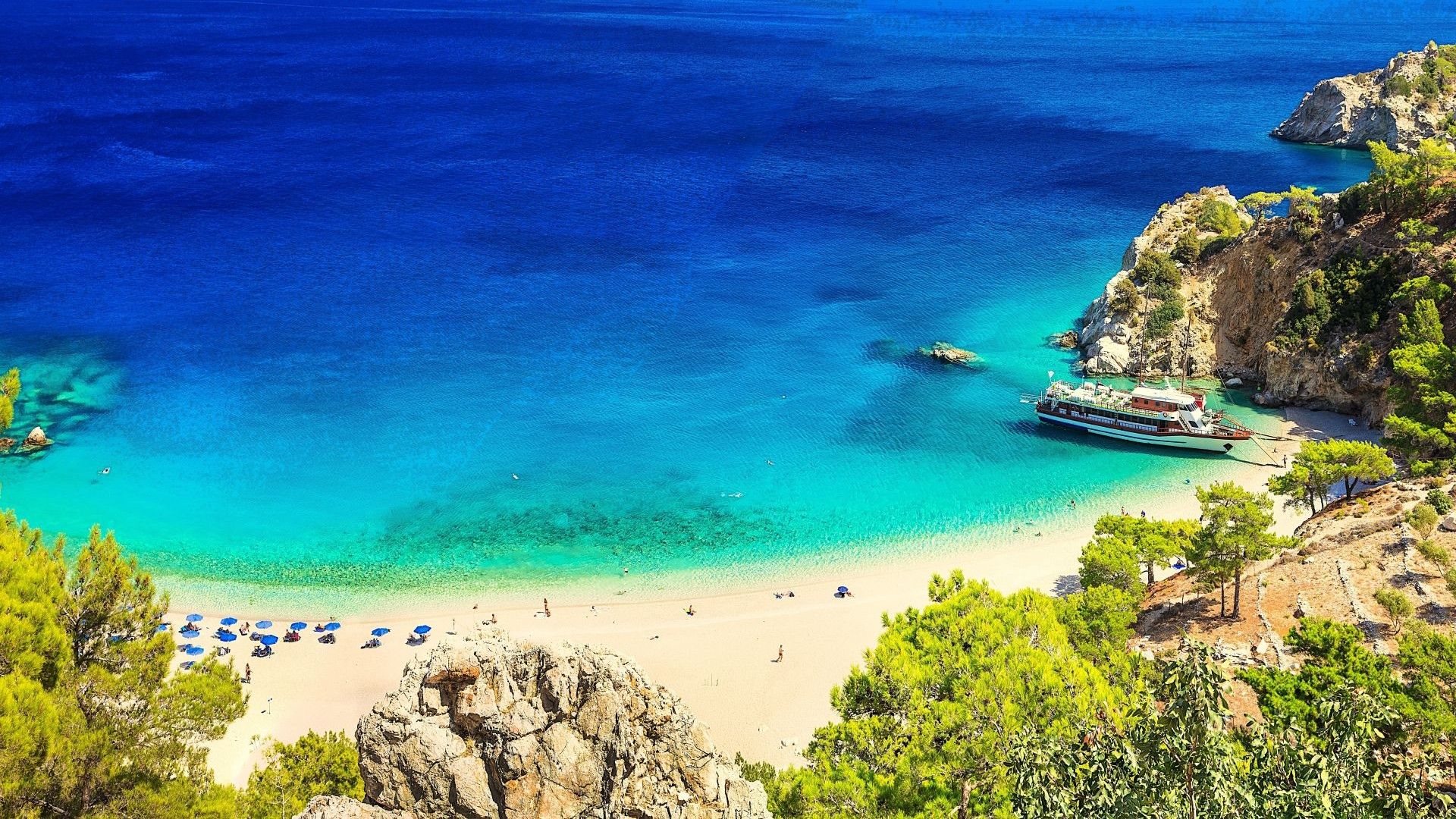 Blick auf eine Bucht einer griechischen Insel mit Sandstrand und Boot auf klarem, blauen Wasser