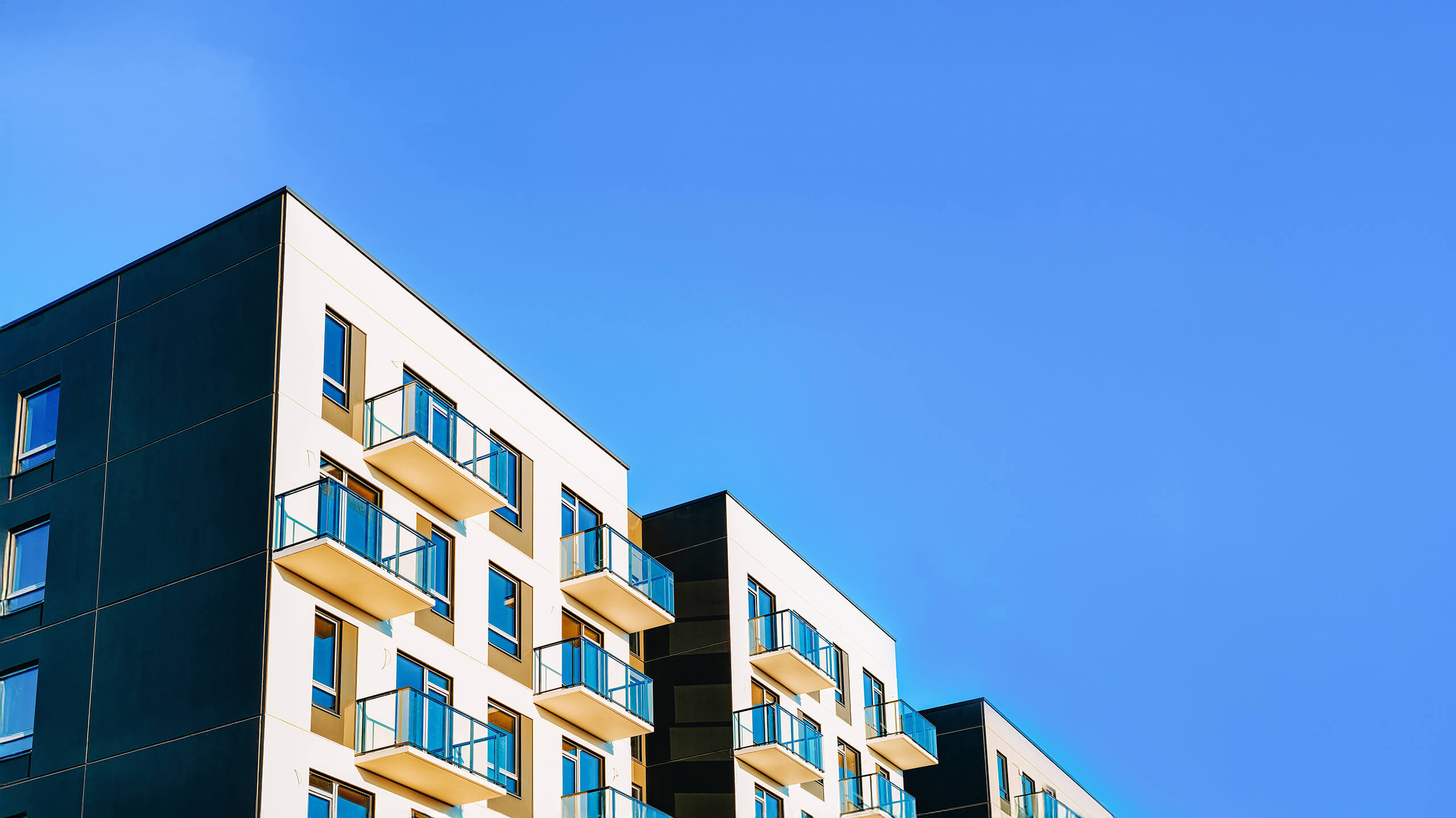 Mehrfamilienhaus mit Balkonen unter klarem blauen Himmel, niedriger Winkel.