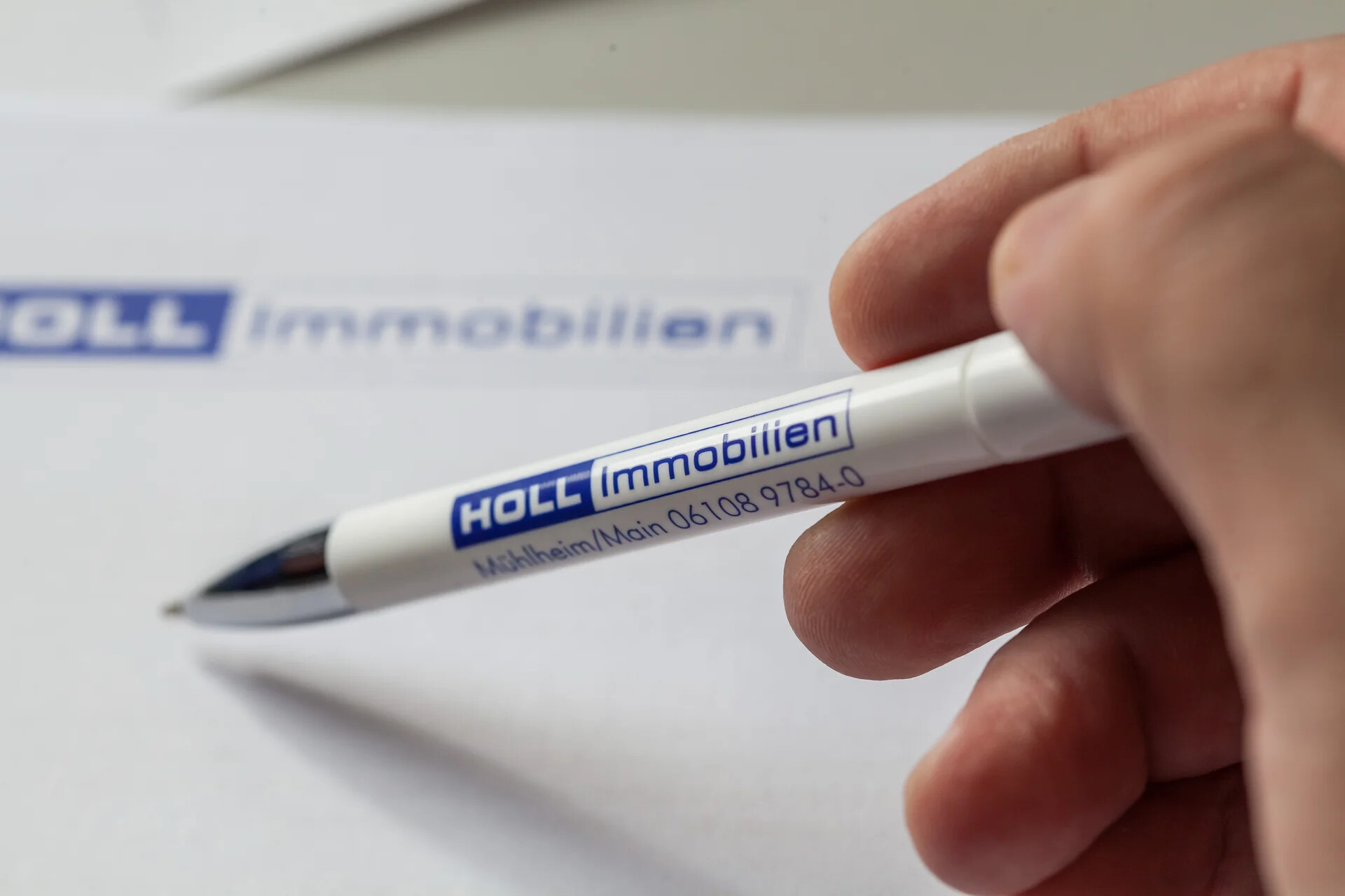 Kugelschreiber mit dem Logo von HOLL Immobilien in einer Hand.