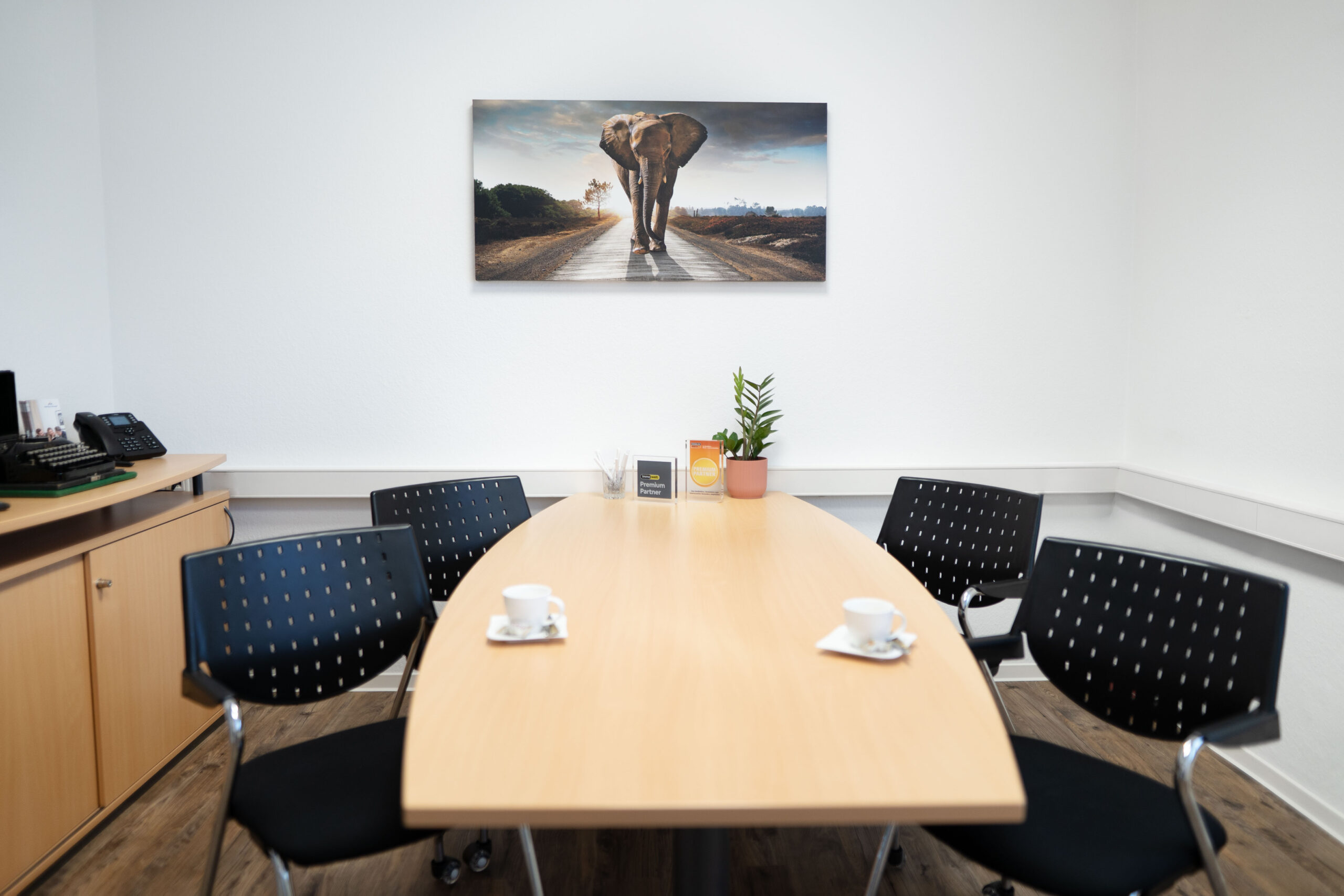 Besprechungstisch mit Kaffeetassen und Elefantenbild an der Wand.