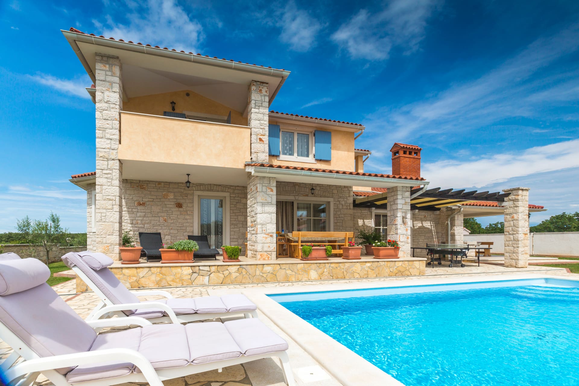 Steinhaus mit Terrasse, Liegestühlen und Pool unter blauem Himmel