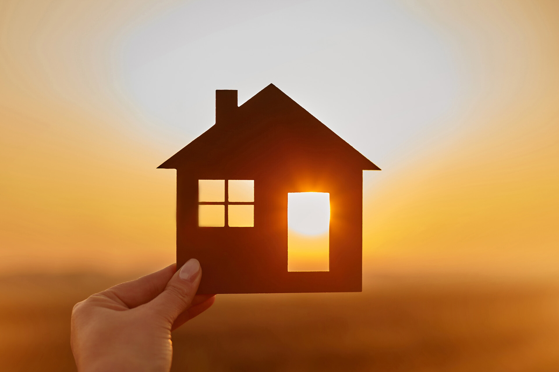 Hand hält ein Haus ausschneide vor Sonnenuntergang, Licht scheint durch