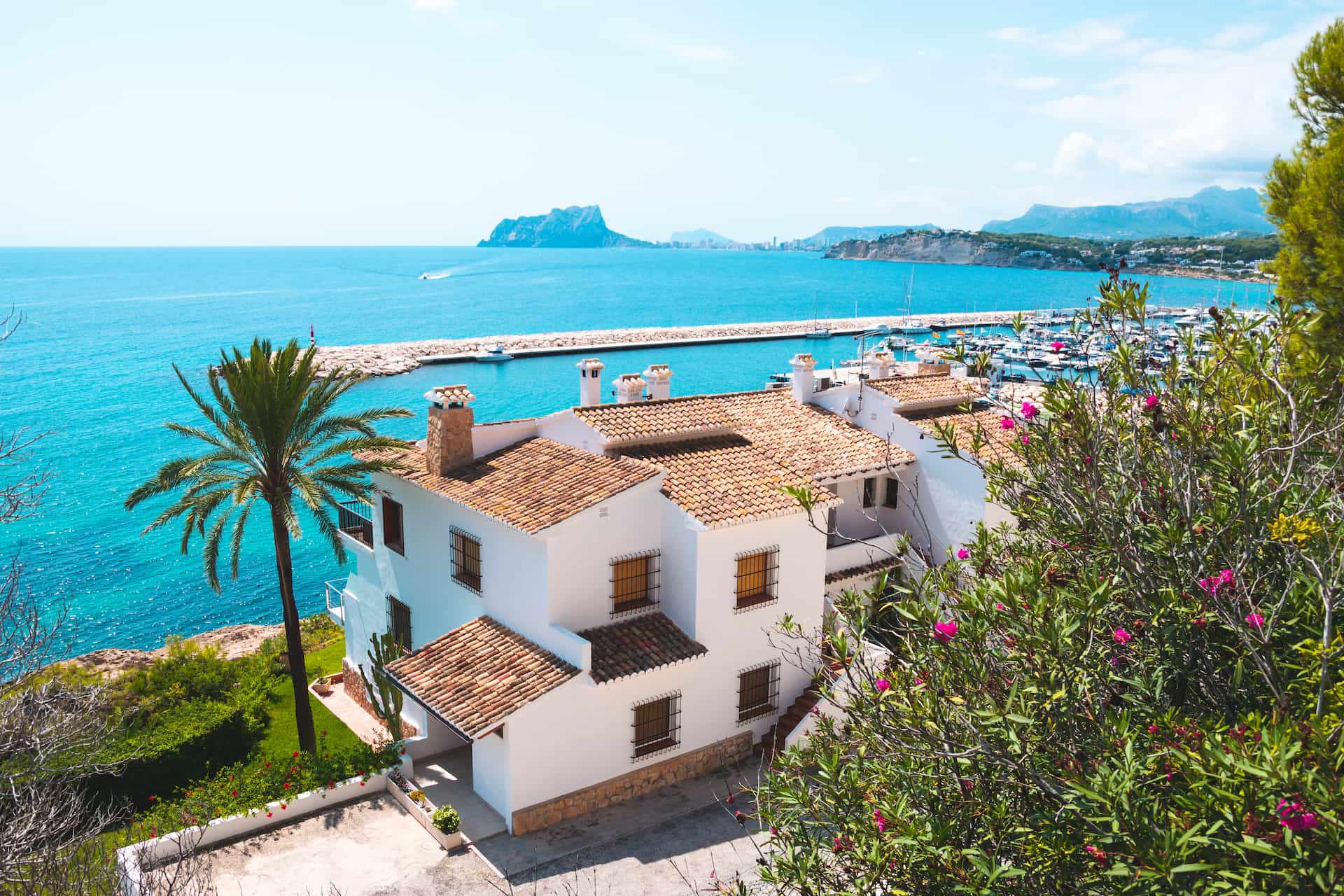 White Mediterranean house by the sea with palm trees, marina and blue sky
