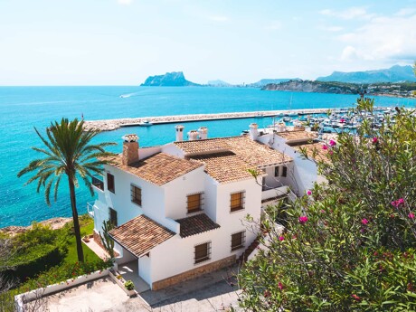White Mediterranean house by the sea with palm trees, marina and blue sky