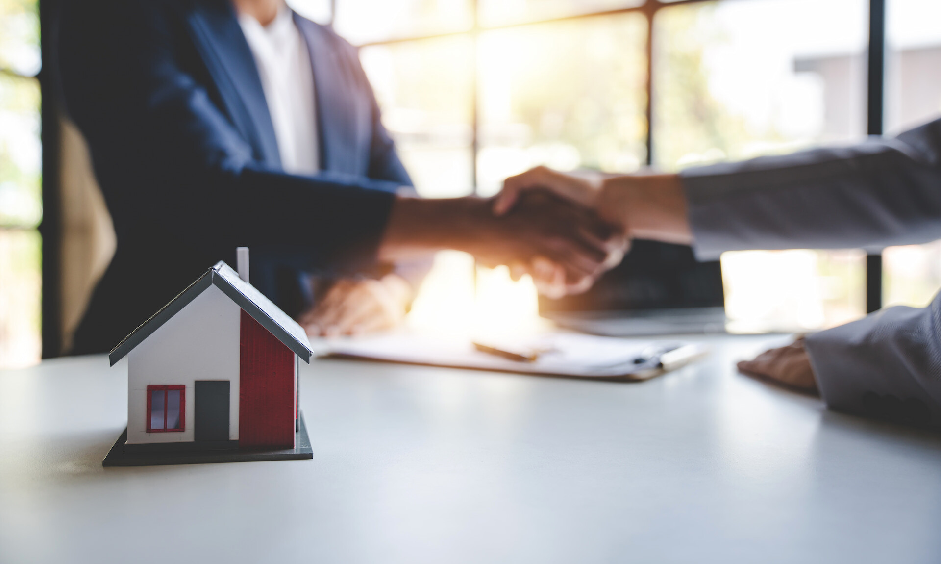 Hausmodell auf Schreibtisch, zwei Menschen reichen sich die Hand