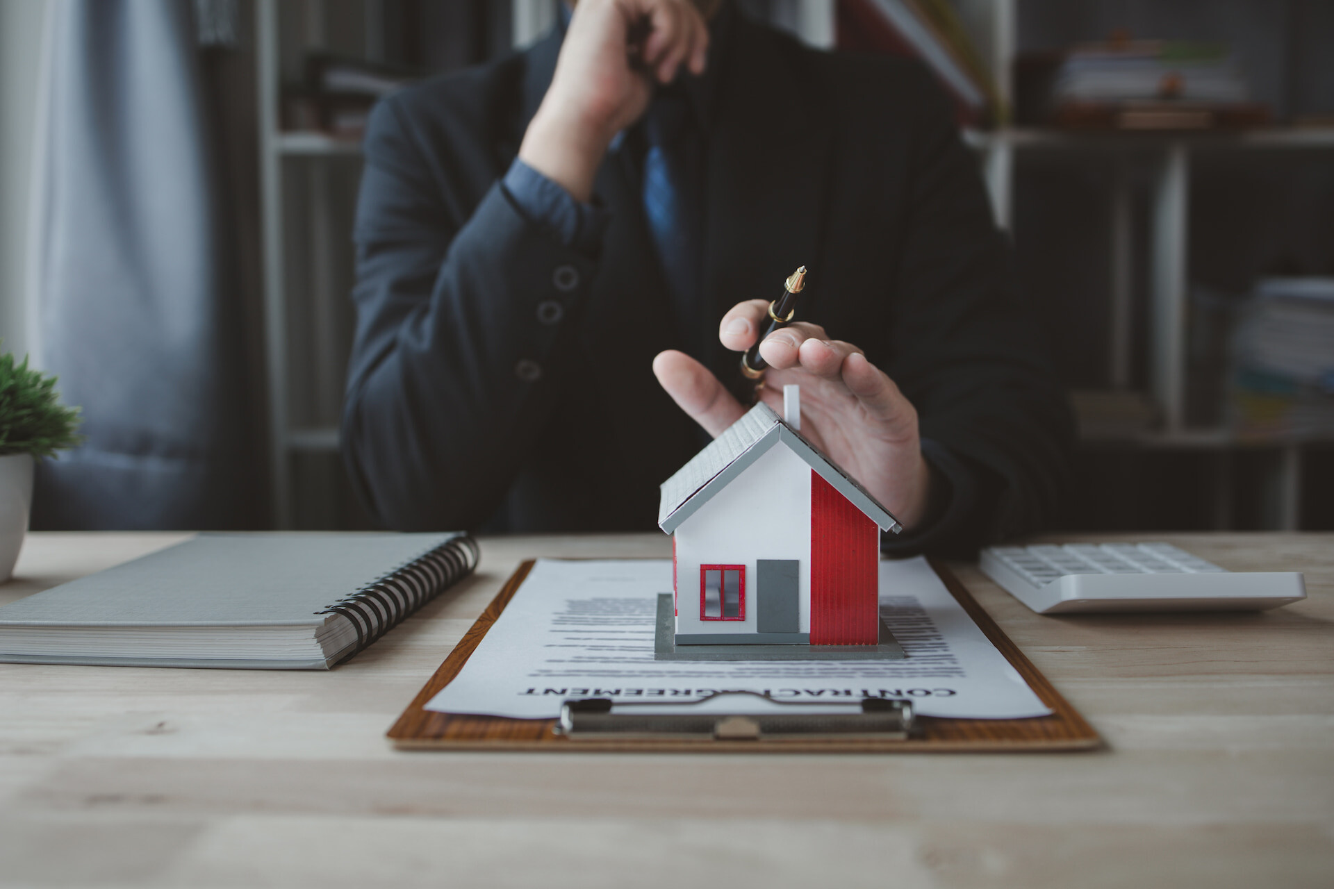 Person im Anzug mit Hausmodell, Vertrag und Schlüssel am Schreibtisch