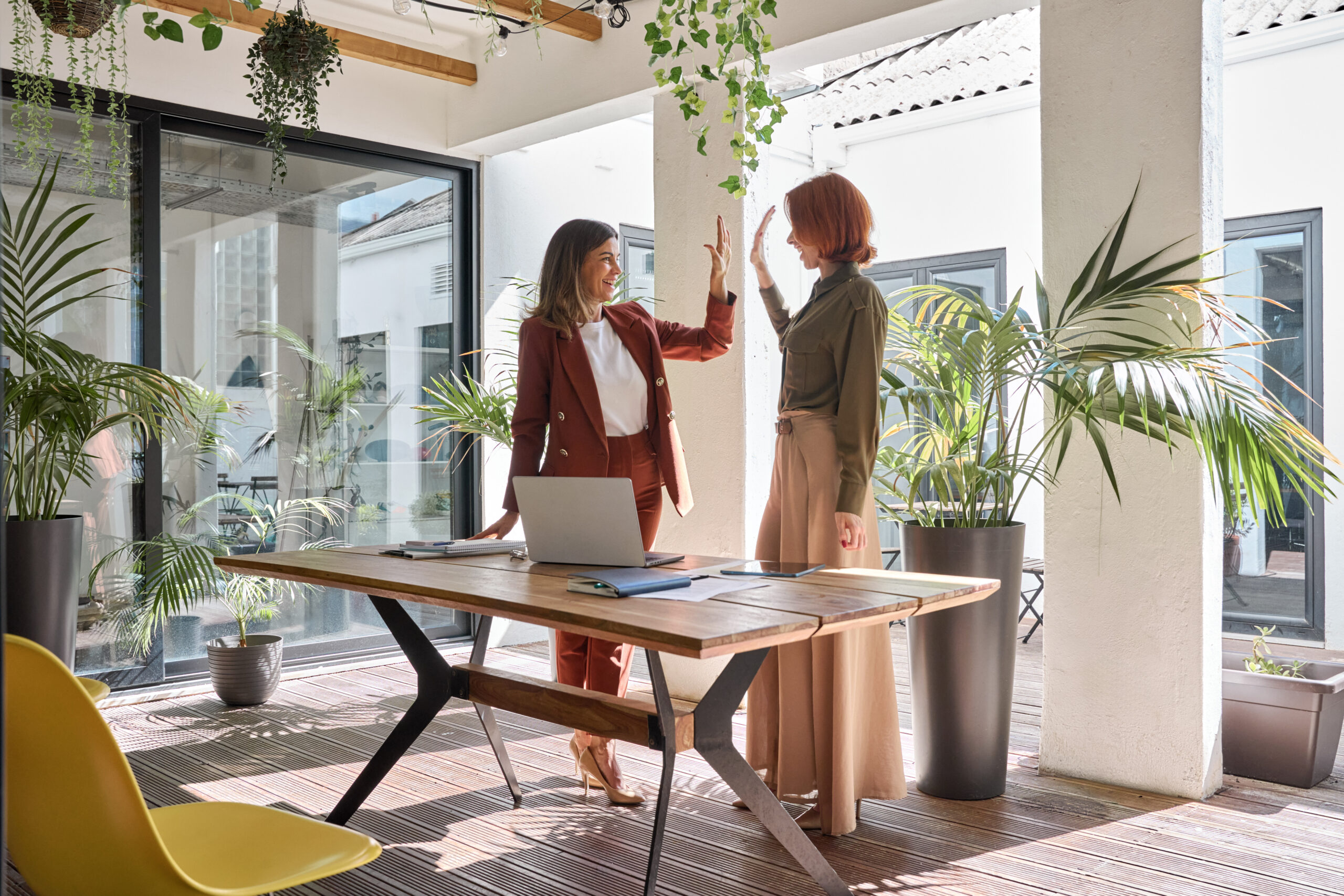 Glückliche, berufstätige Geschäftsfrauen feiern ihren Erfolg mit einem High Five im Büro.