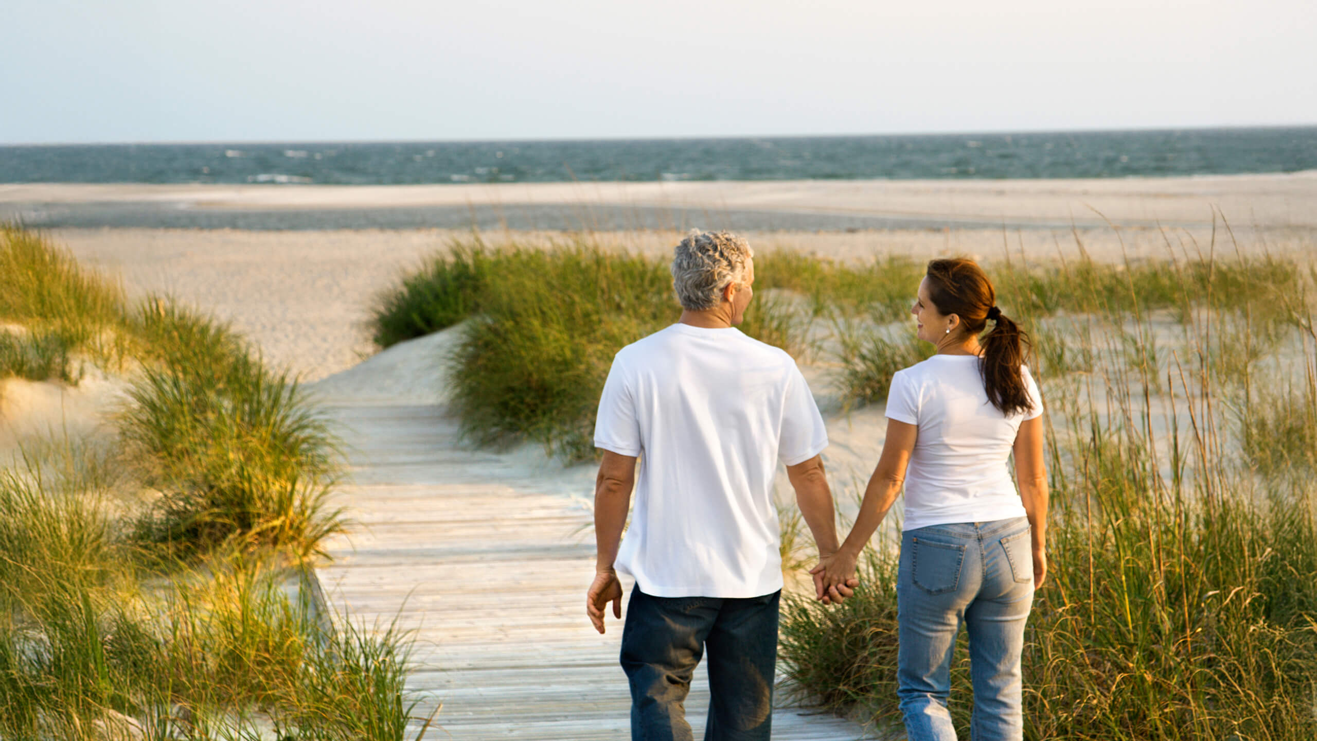 Ein Paar läuft barfuß Hand in Hand auf einem sonnigen Strandweg