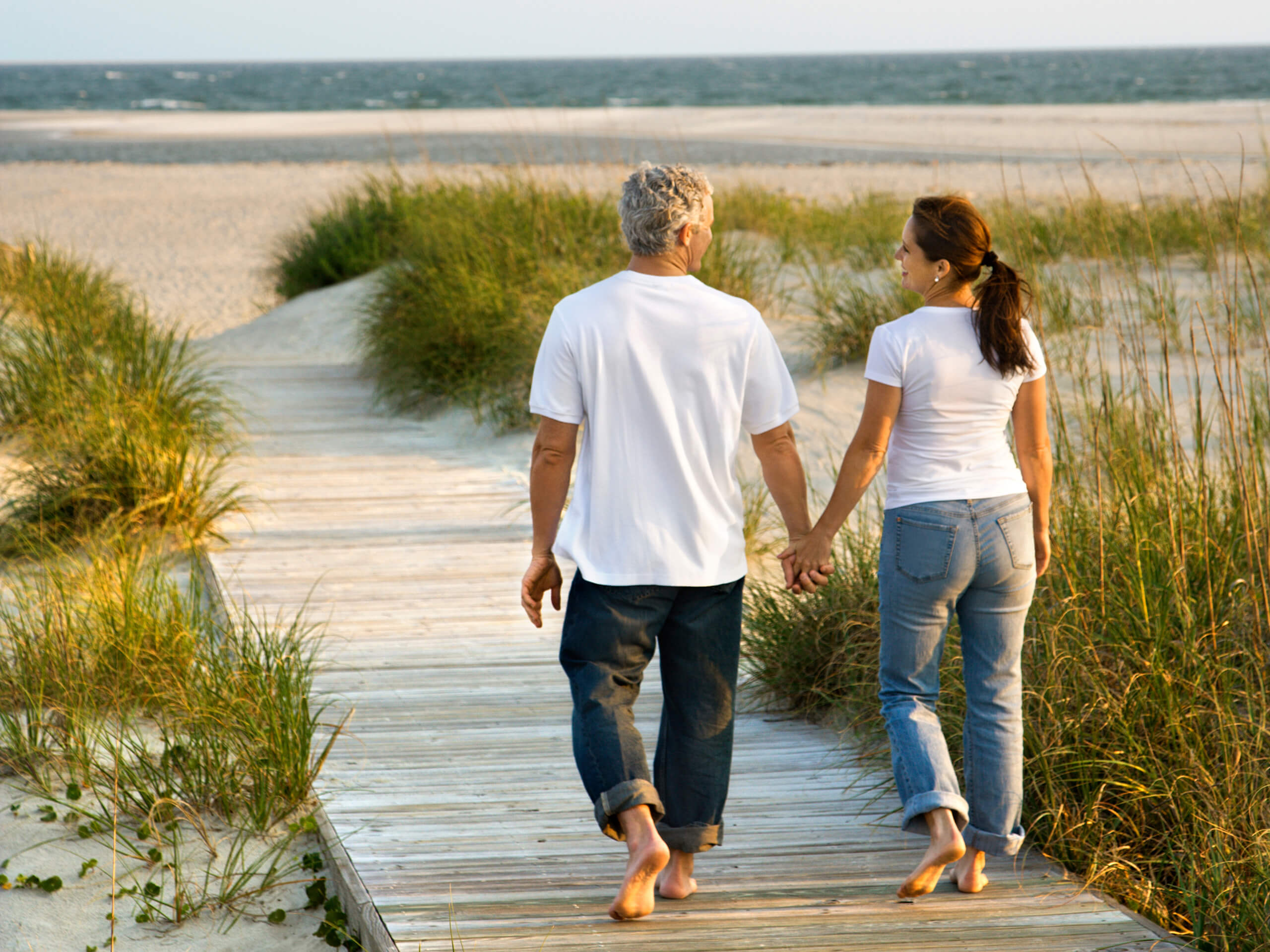 Ein Paar läuft barfuß Hand in Hand auf einem sonnigen Strandweg