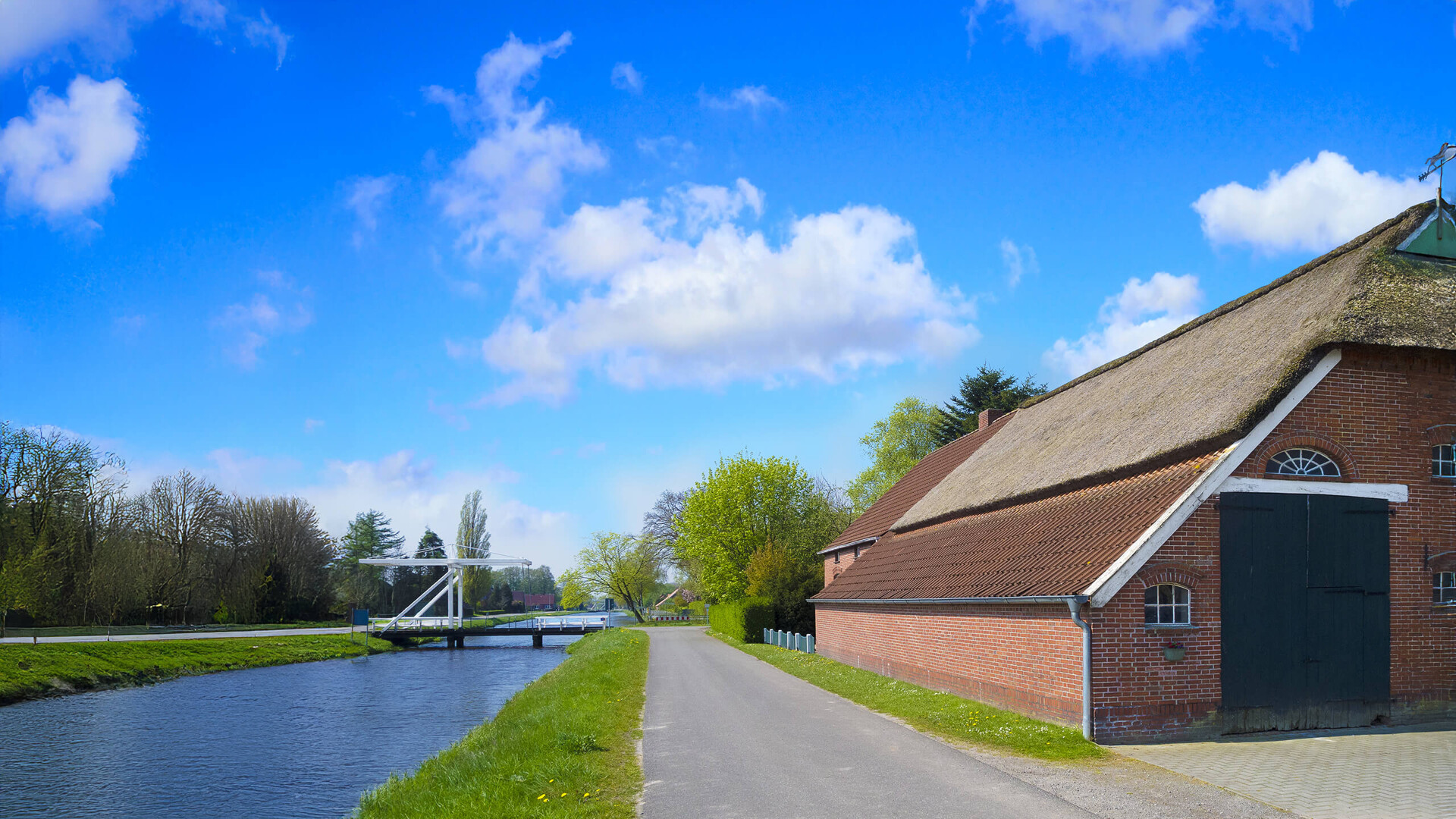 Landstraße, Kanal, roter Ziegelbau mit Strohdach unter Wolken