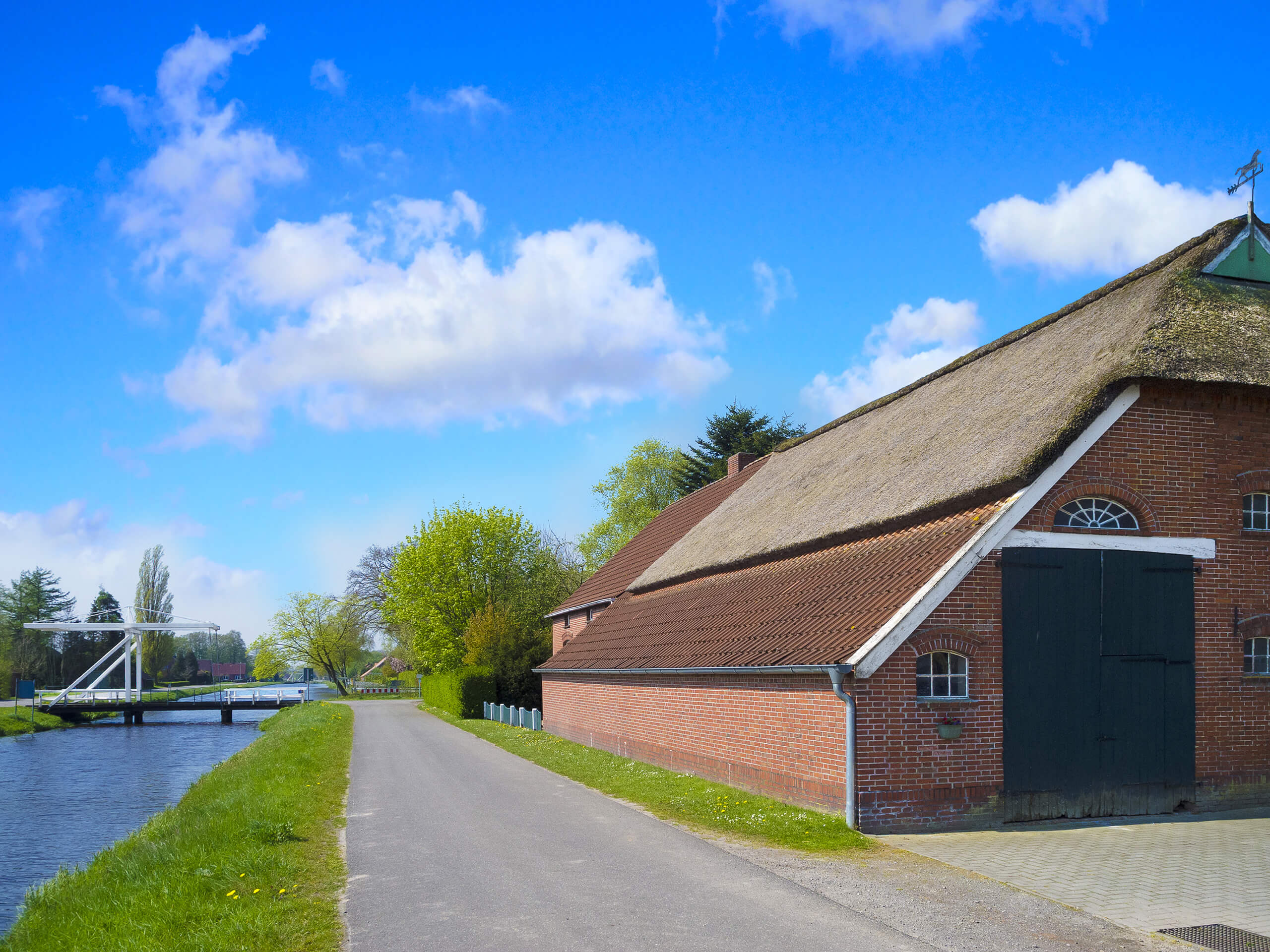 Landstraße, Kanal, roter Ziegelbau mit Strohdach unter Wolken