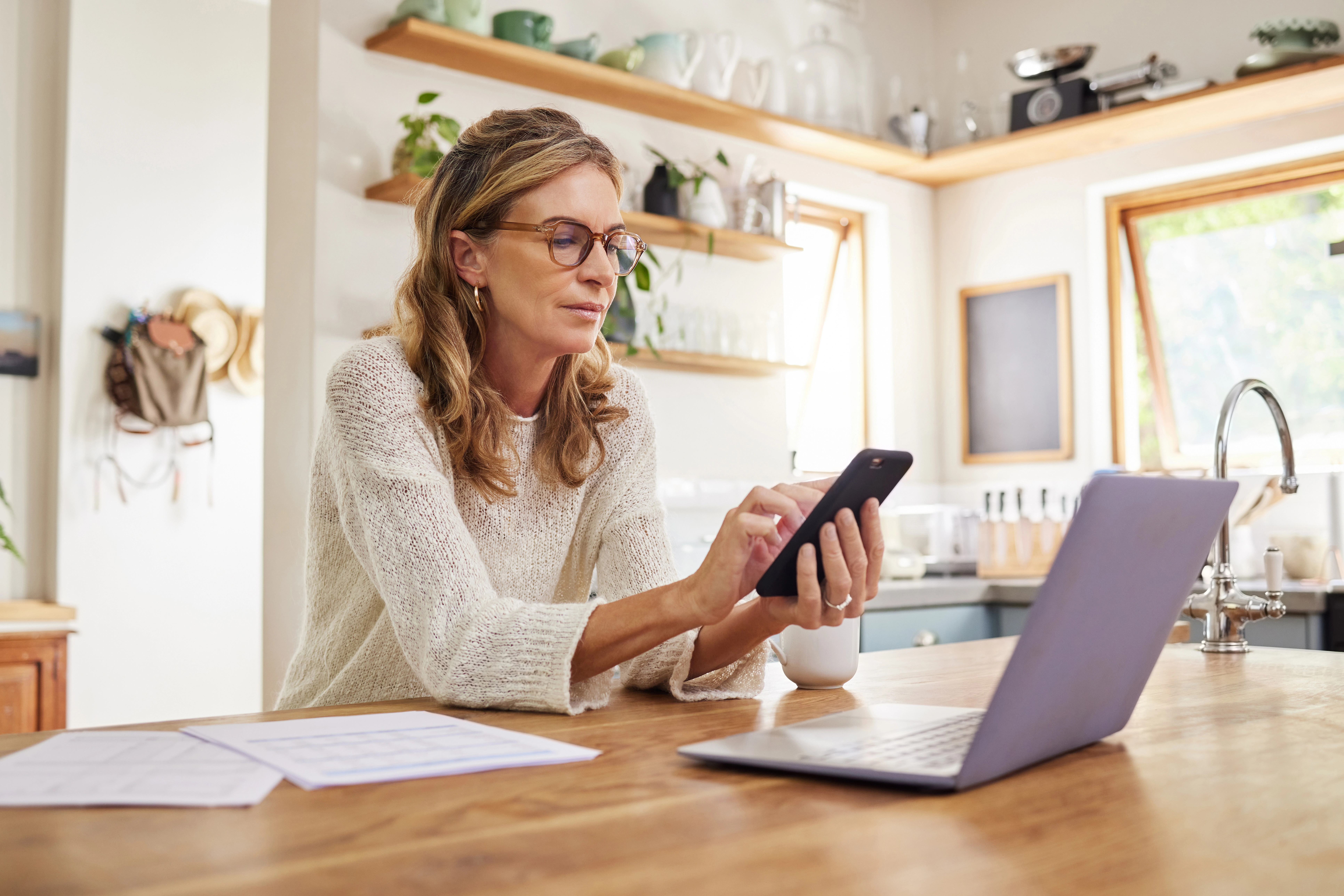 Frau mit Laptop vor sich bedient Smartphone