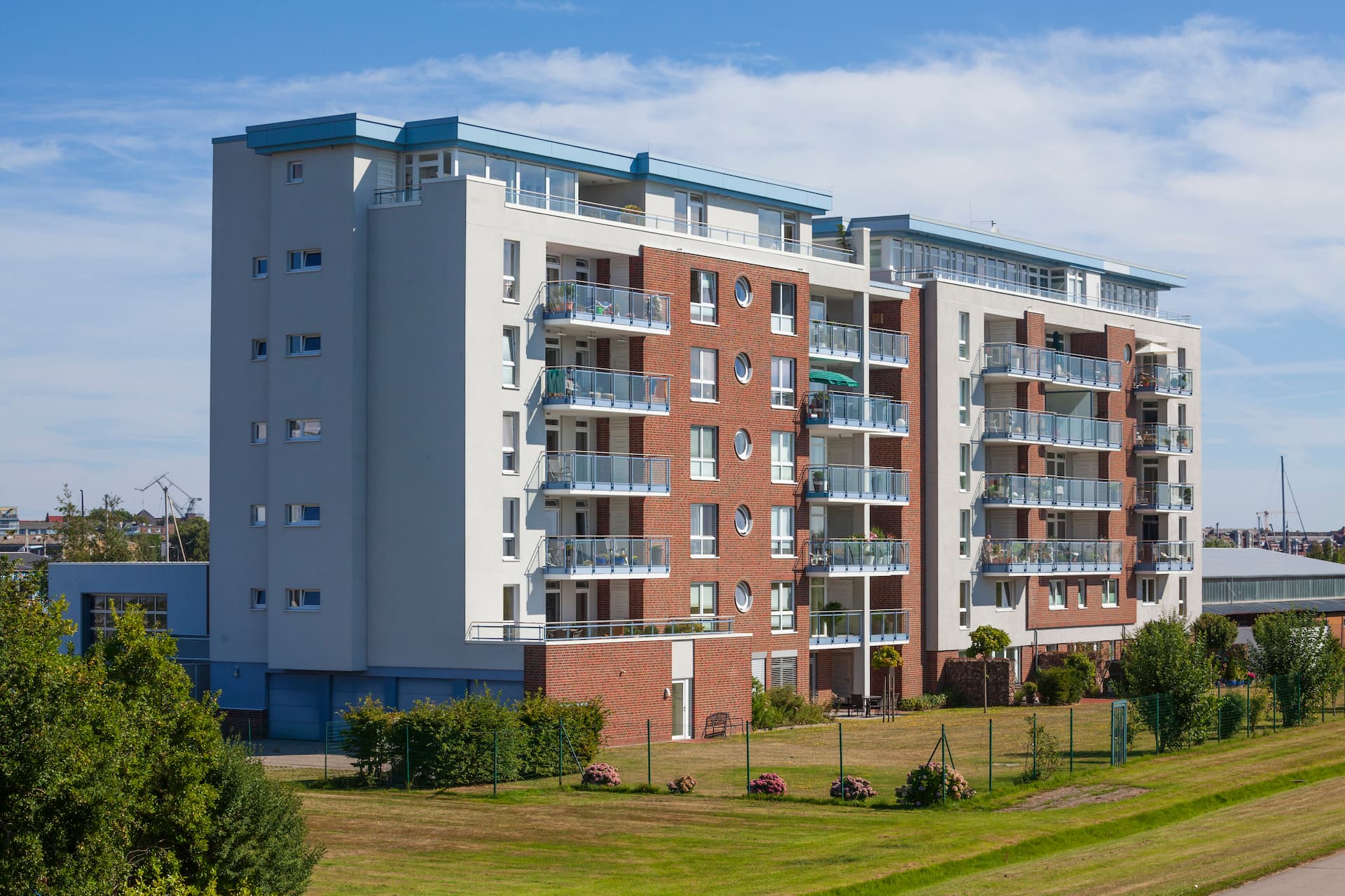 Mehrfamilienhaus mit Balkonen und Gras unter blauem Himmel.