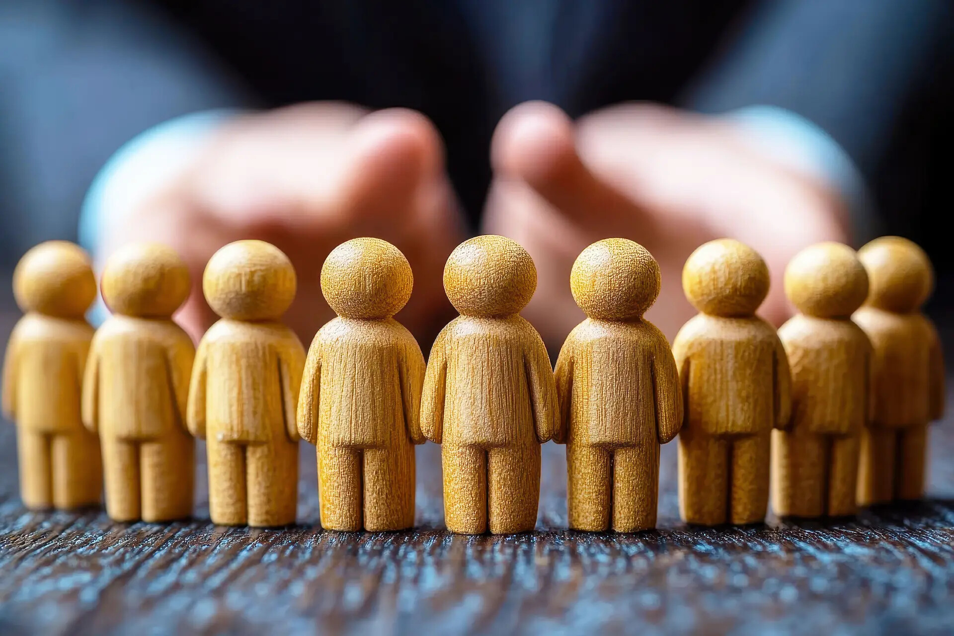 Holzfiguren in Reihe, Hände darüber zum Schutz oder Führen.