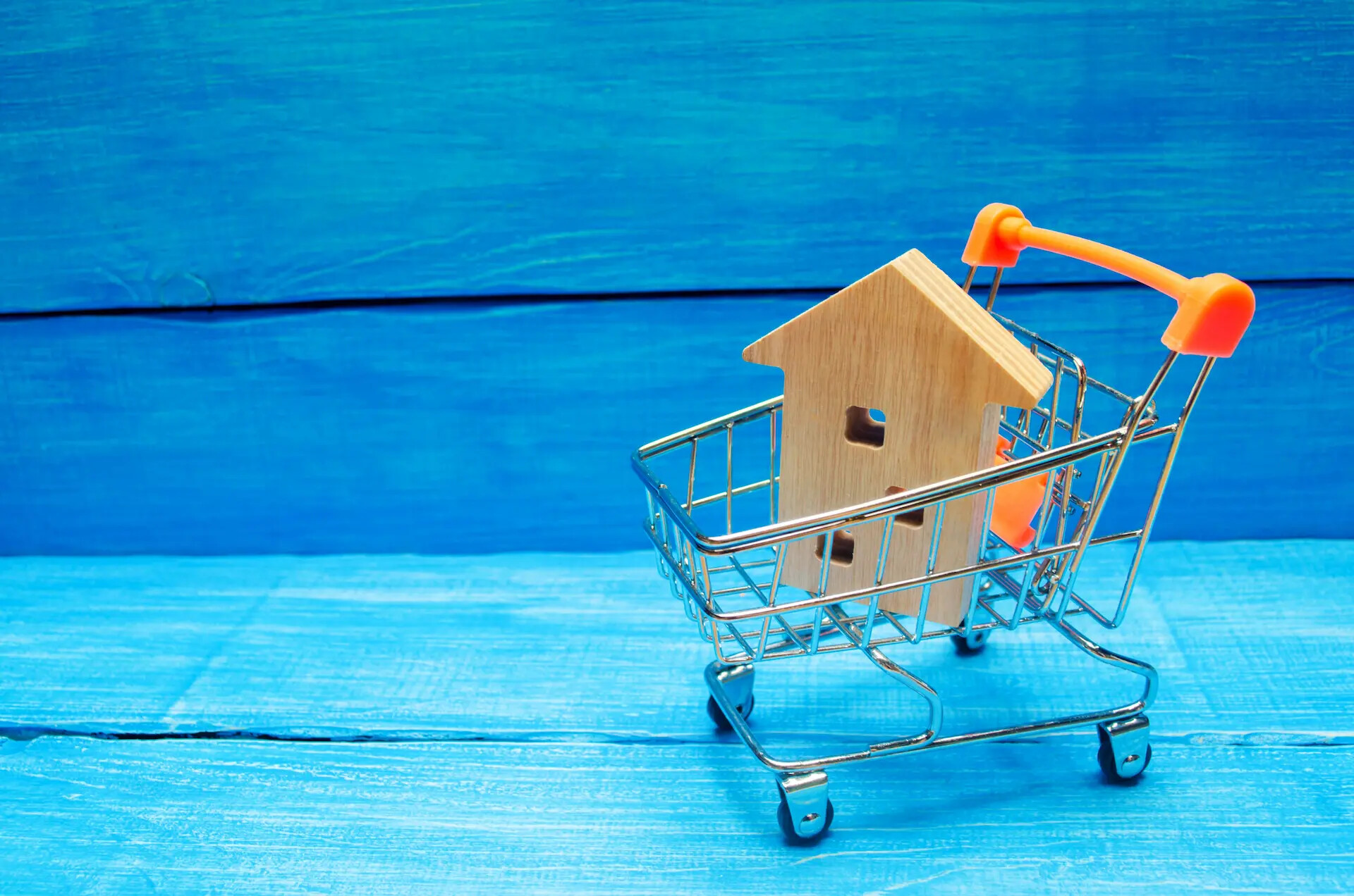 Holzhaus in einem Einkaufswagen auf blauem Holzhintergrund.