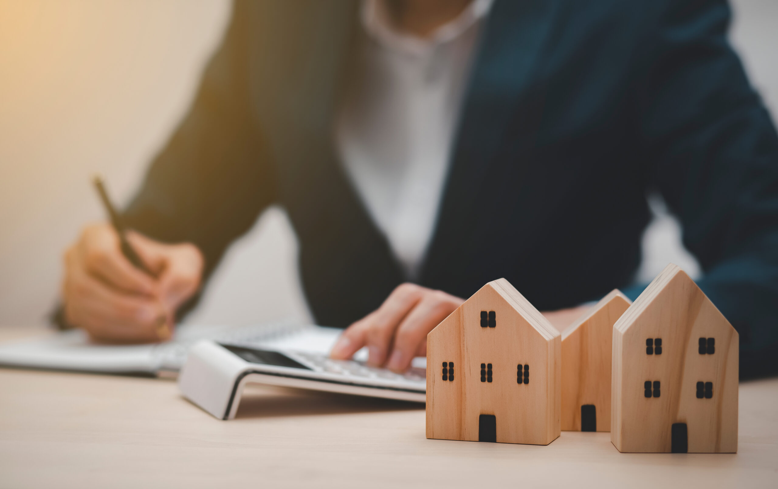 Person mit Taschenrechner, kleine Holzhäuser auf Schreibtisch.