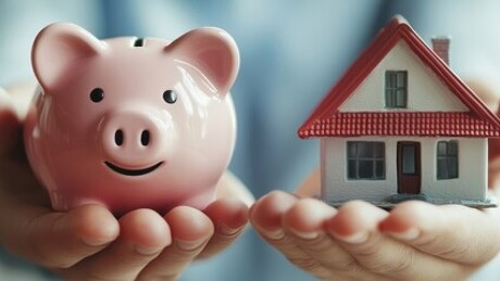 Eine Person hält beide Hände ausgestreckt, auf einer steht ein Sparschwein, auf der anderen ein Modellhaus.